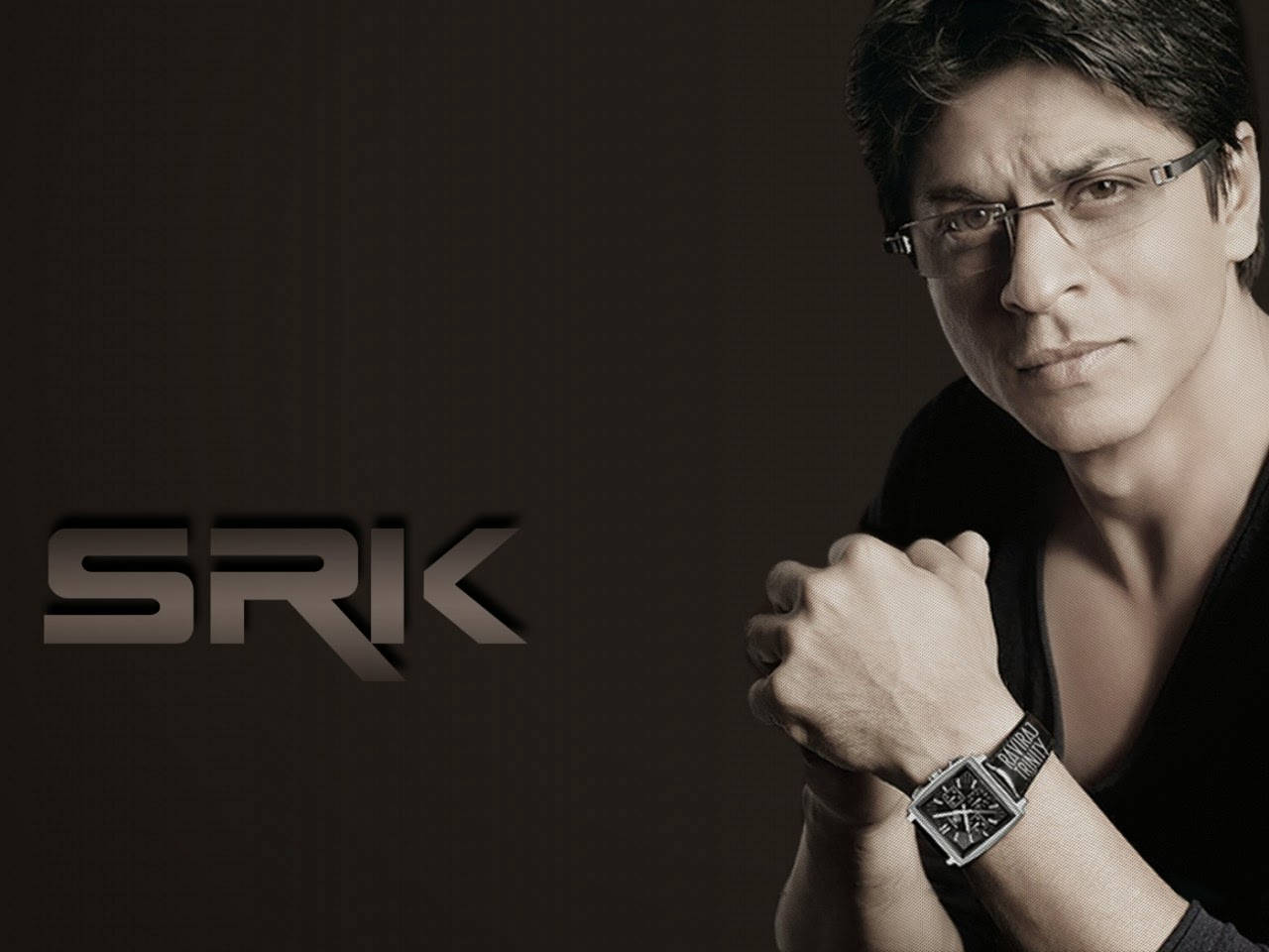 Shahrukh 桌布 壁紙 — 一名戴眼鏡和手錶的男子在帶有'SRK'標誌的深色背景前凝視。