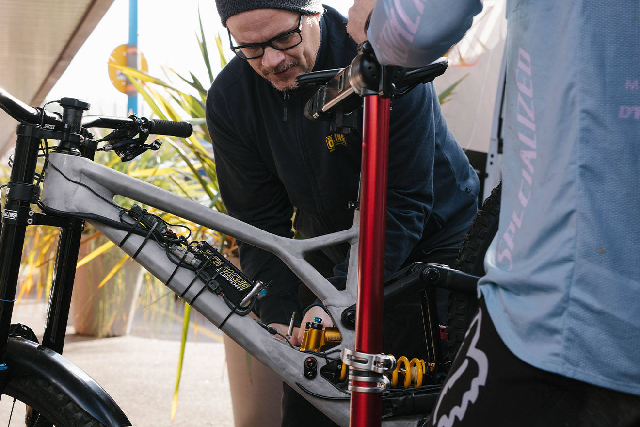 腳踏車 桌布 壁紙 — 一名戴眼鏡和毛帽的男子在明亮的日光下仔細調整高科技登山車的避震系統。