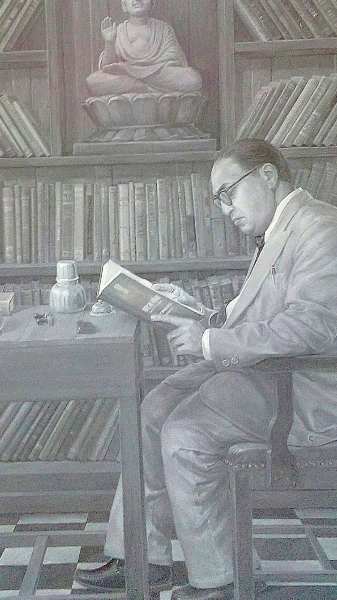 桌布 壁紙 — 一名戴眼鏡的男子在寧靜的圖書館書桌前閱讀一本書，身後有書架和一尊佛像。