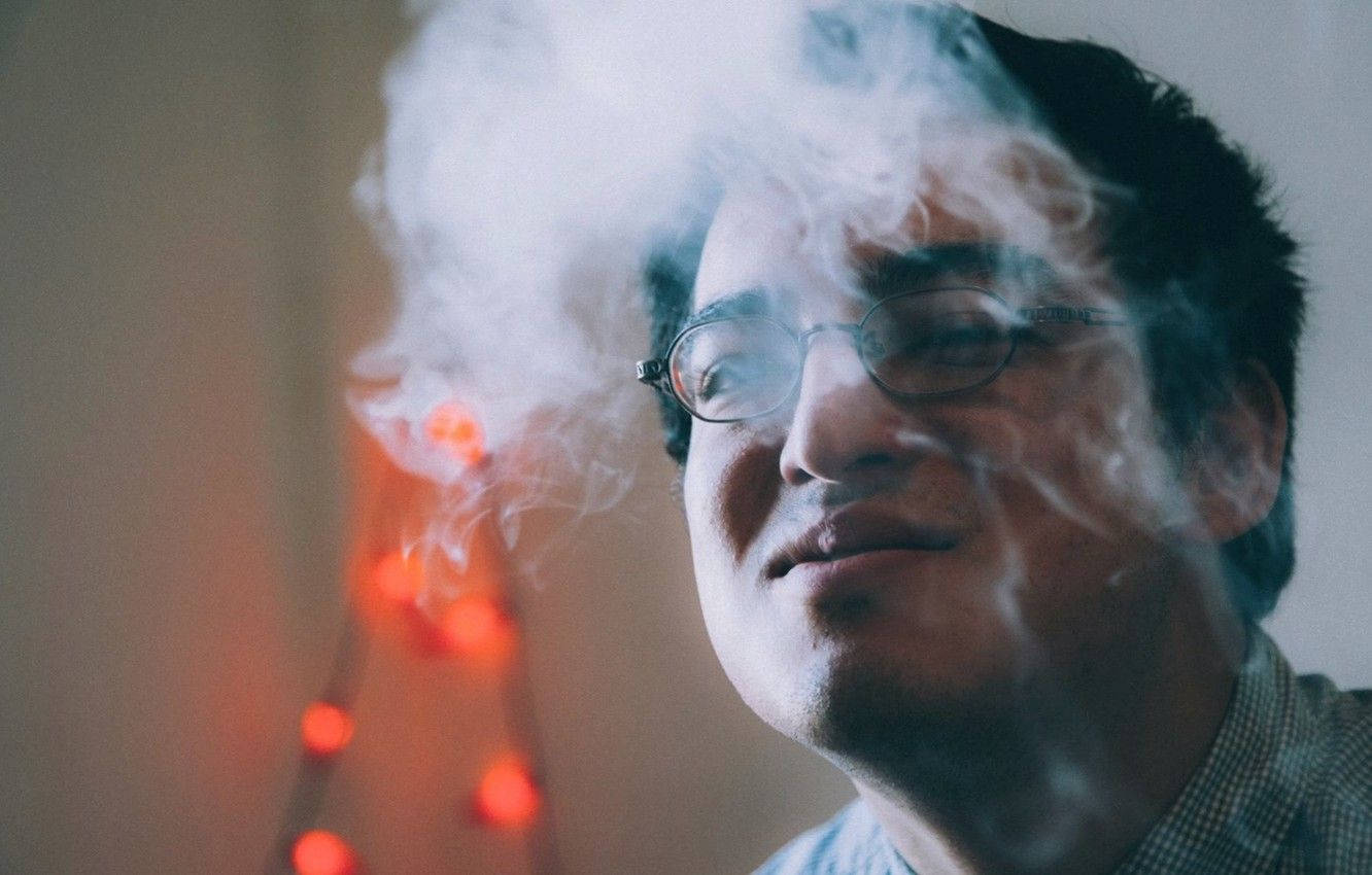 filthy frank 桌布 壁紙 — 一名戴眼鏡的男子在溫暖發光的燈串背景下呼出一團濃煙。