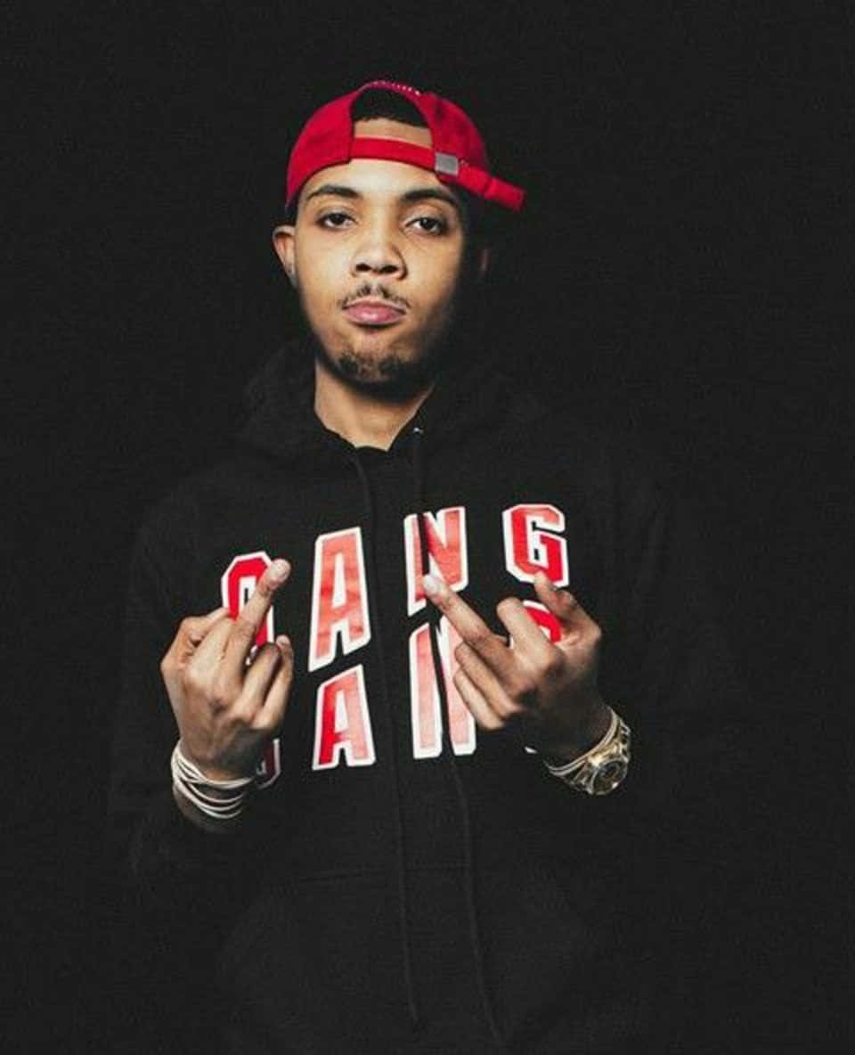 Herbo iPhone 桌布 壁紙 — 一名戴紅色帽子、身穿印有紅色字樣的黑色連帽上衣的年輕男子，在深色背景前做出手勢。