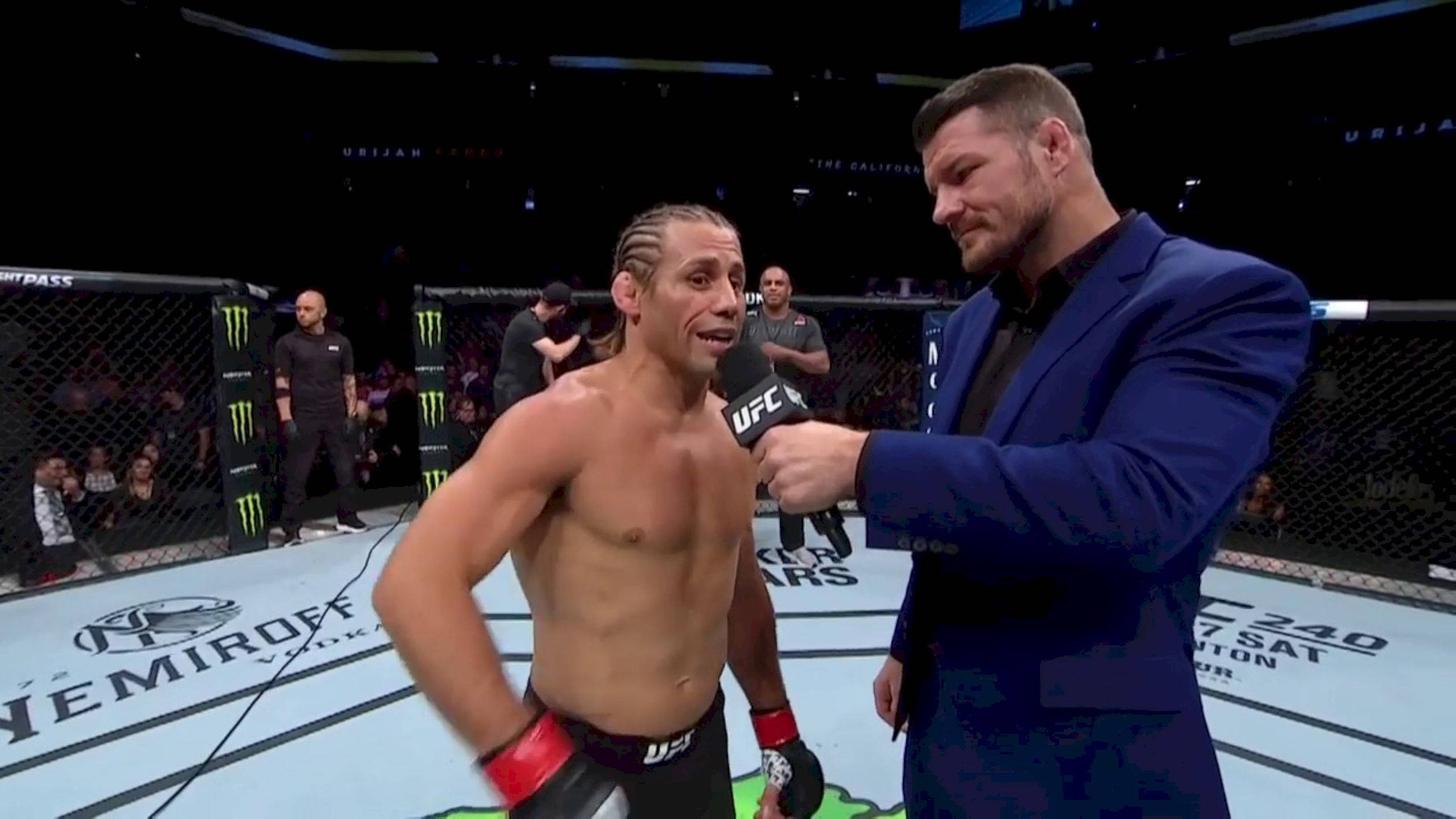 UFC 桌布 壁紙 — 一名戴紅色手套的UFC拳手在燈光明亮的八角籠內接受一名穿藍色西裝的男子訪問，觀眾和品牌標誌清晰可見。