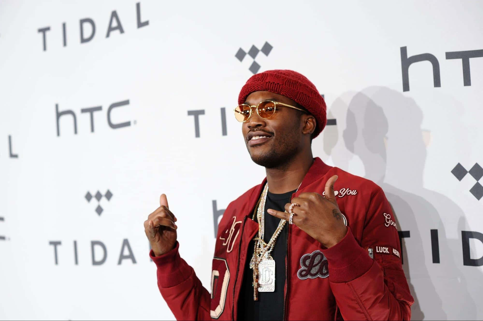Meek 桌布 壁紙 — 一名戴紅色毛帽和穿紅色外套的男子在TIDAL活動中自信地做手勢，背景有品牌標誌。