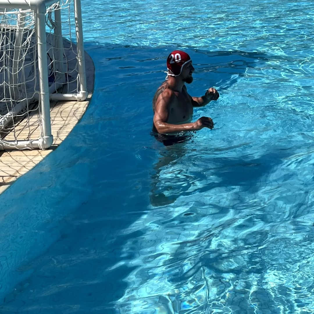 Swimming 桌布 壁紙 — 一名戴紅色泳帽、編號20的水球運動員站在陽光普照下、白色球門網附近的明亮藍色泳池中。