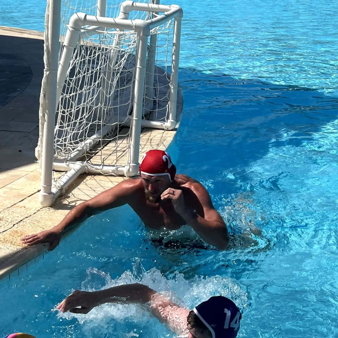 Swimming 桌布 壁紙 — 一名戴紅色泳帽的水球運動員衝向球門，另一名運動員在充滿活力的藍色泳池中游過。