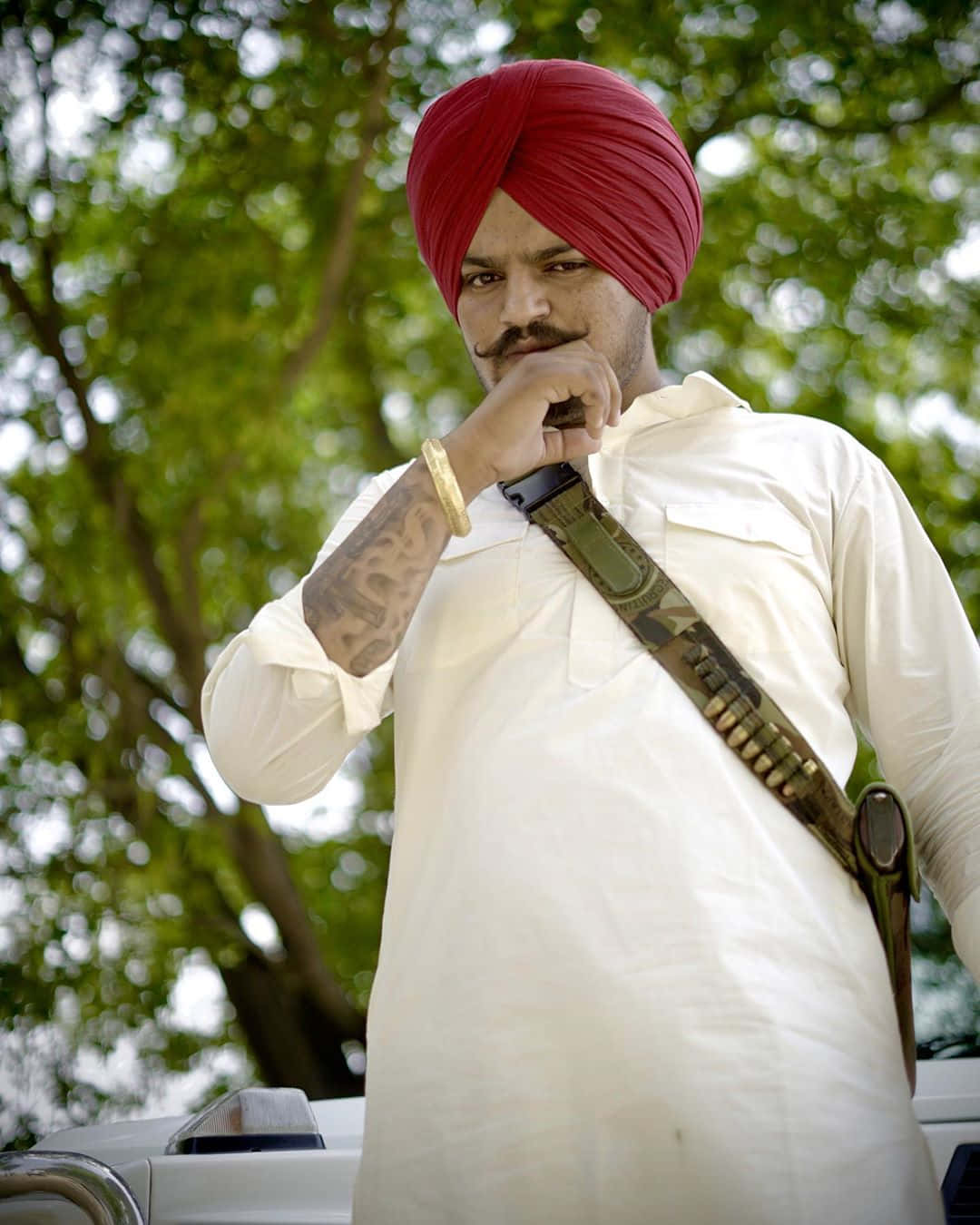 戴紅色頭巾、身穿白衫的男子在戶外拿著步槍帶。 — Sidhu Moose Wala 壁紙