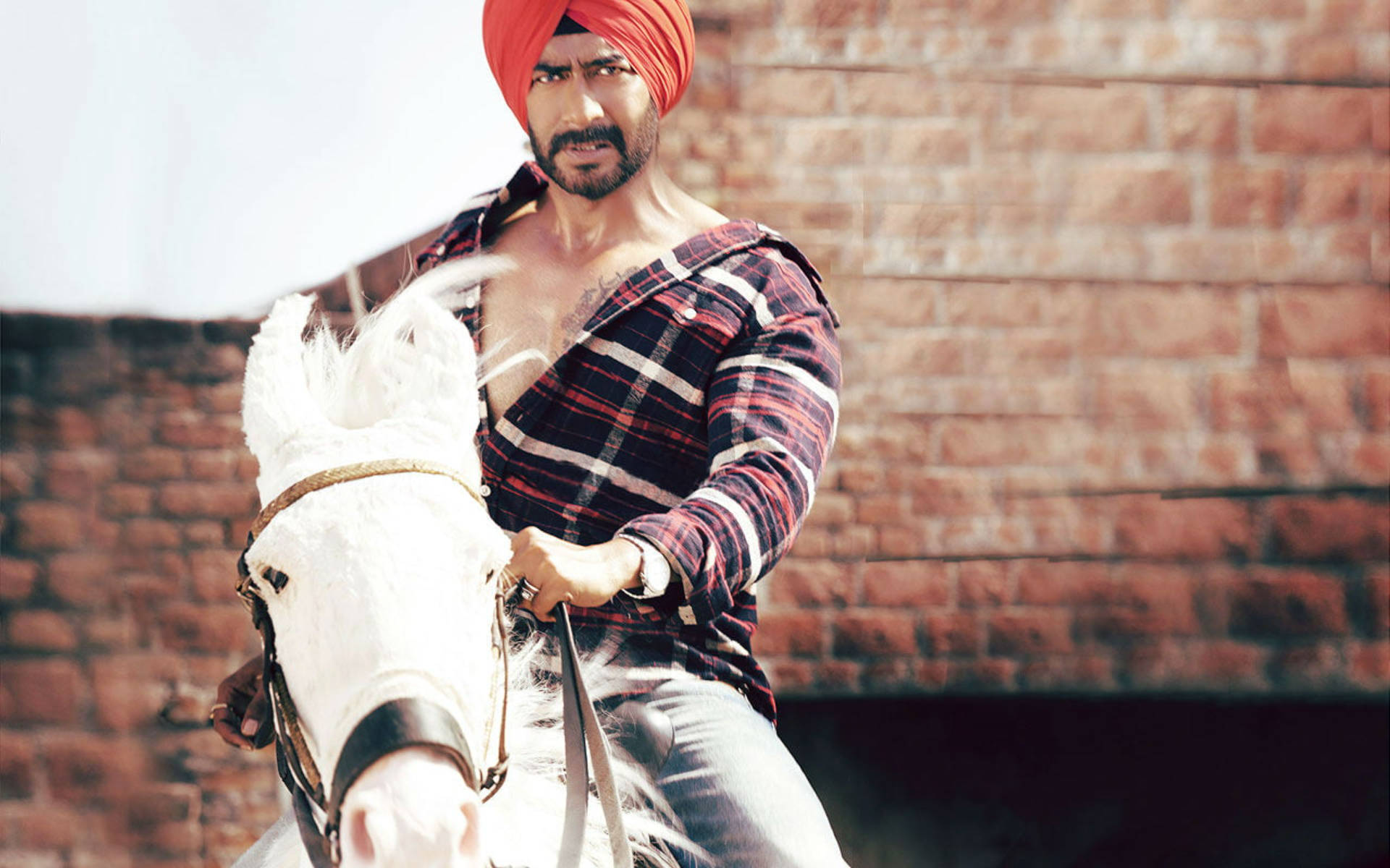 ajay devgn 桌布 壁紙 — 一名戴紅色頭巾的男子騎著一匹白馬，在陽光照射的磚牆前，神情專注。