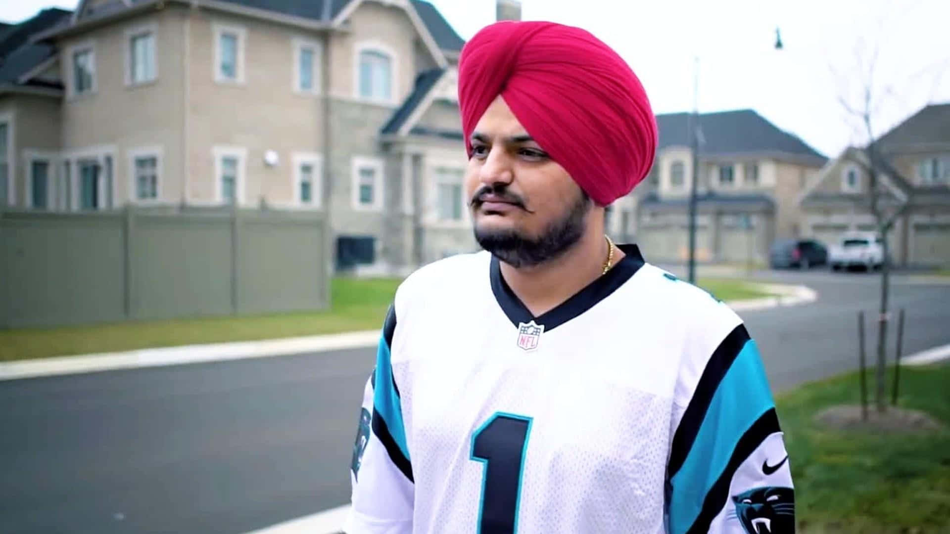 戴紅頭巾的男子站在房屋前 — Sidhu Moose Wala 壁紙