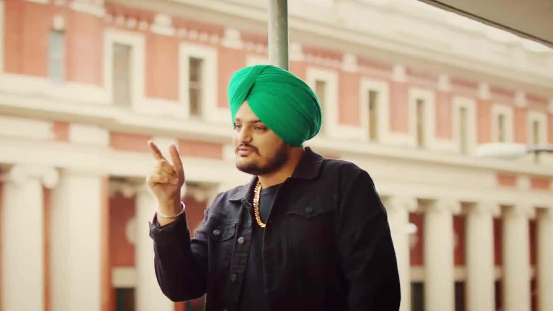 戴綠色頭巾的男子指向建築物 — Sidhu Moose Wala 壁紙
