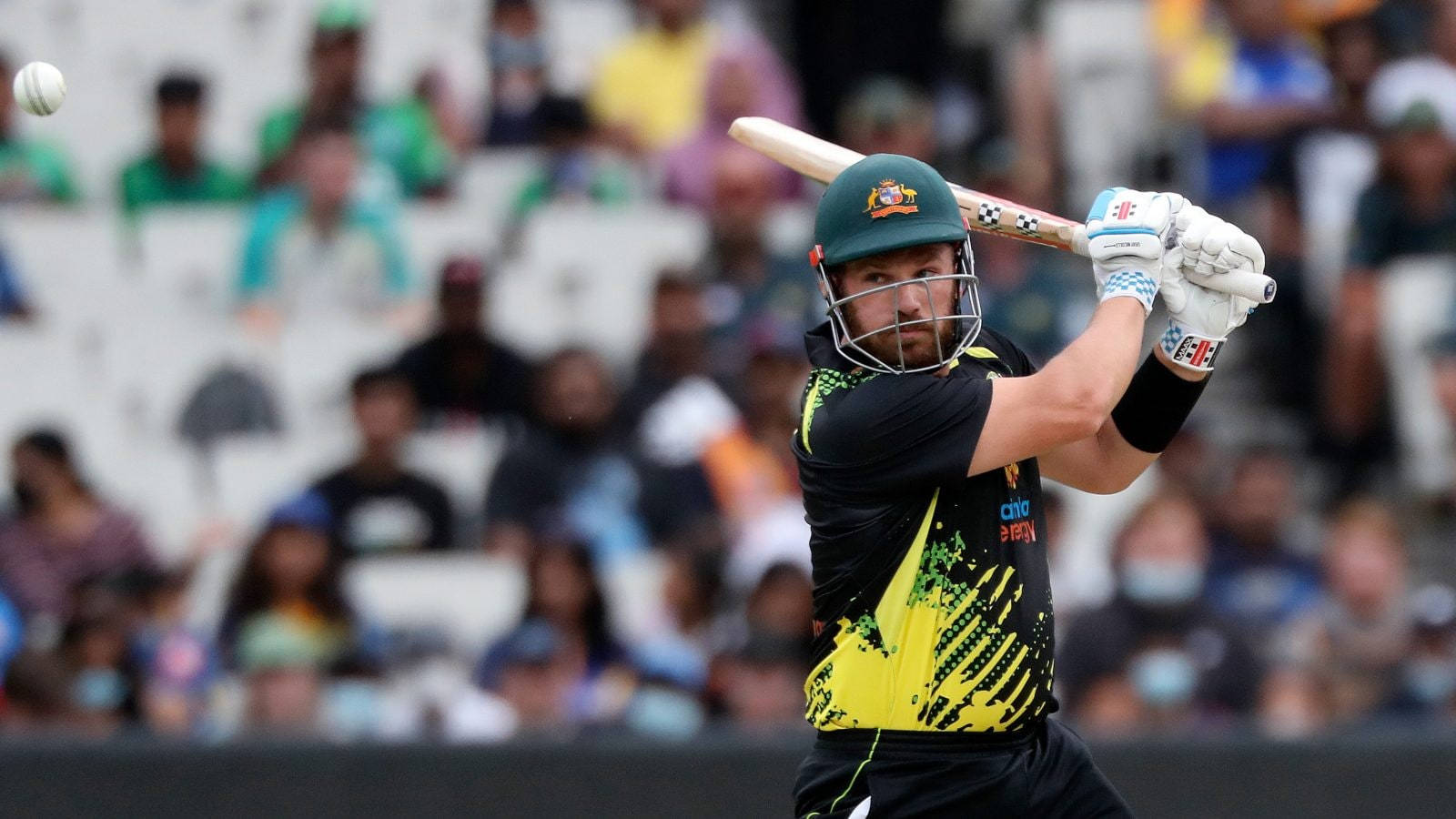 Aaron Finch 桌布 壁紙 — 一名戴綠色頭盔、身穿黑黃球衣的板球擊球手在日間比賽中向空中揮棒擊打白色球。
