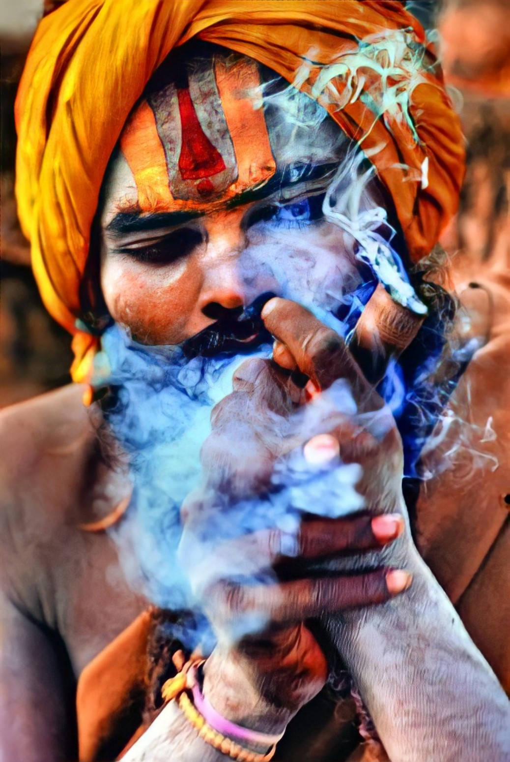 Aghori 桌布 壁紙 — 一名戴著亮橙色頭巾、帶有儀式標記的男子，手持煙斗呼出藍色煙霧的特寫。