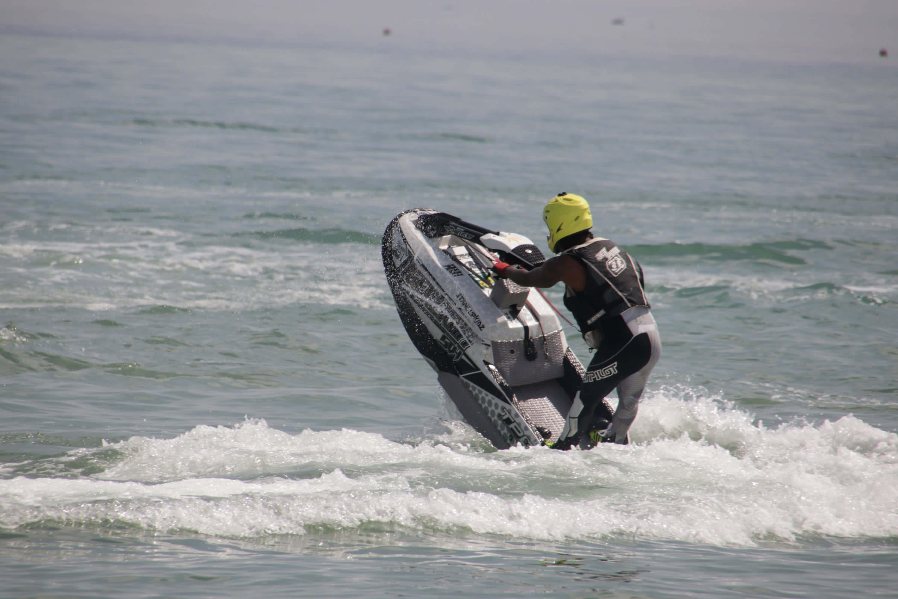 Beach Water Sports 桌布 壁紙 — 一名戴著亮黃色頭盔的滑水運動員在滑水板上傾身轉彎，劃過波濤洶湧的海浪。