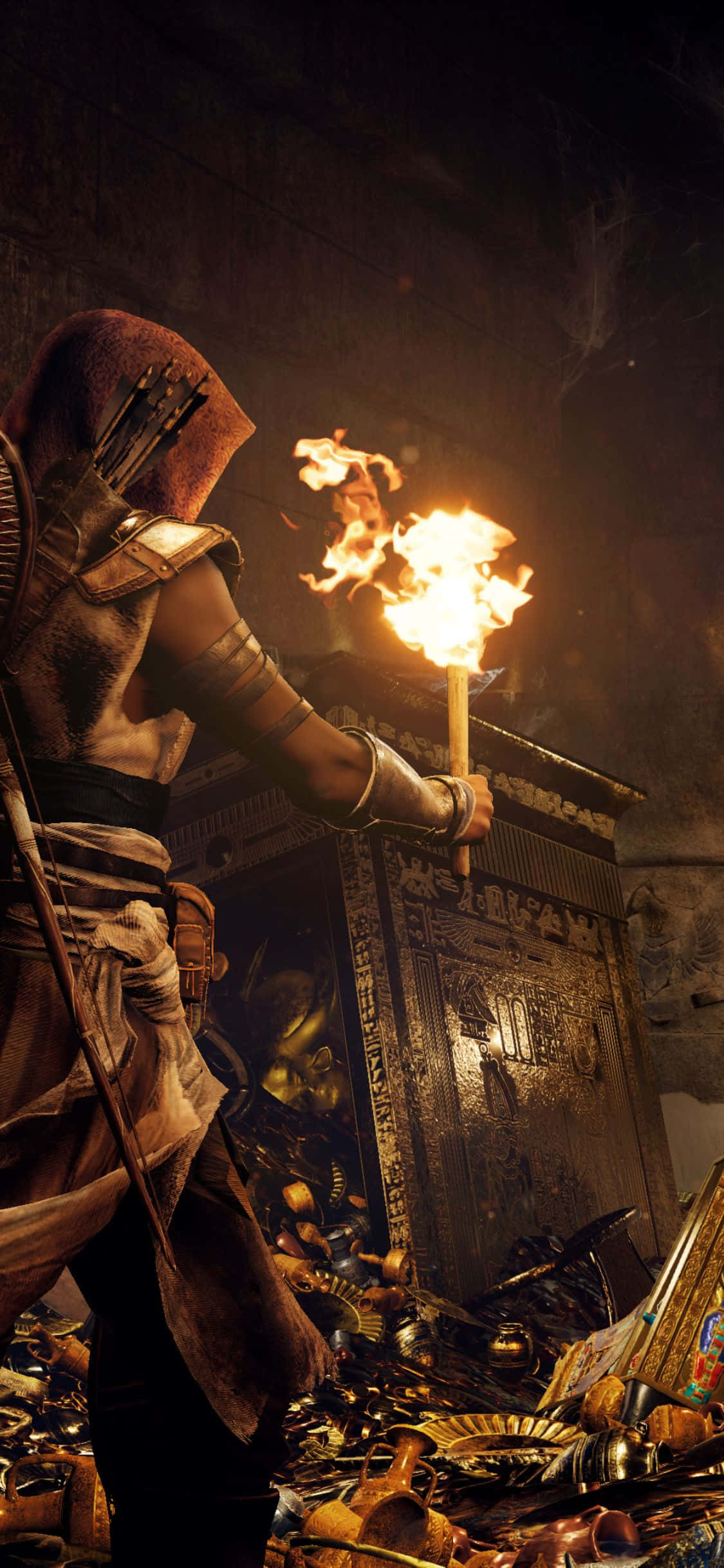 iPhone X Assassin's Creed Origins 桌布 壁紙 — 一名戴著兜帽的刺客在一個光線昏暗、充滿黃金遺物和象形文字的古老墓穴中手持燃燒的火把。