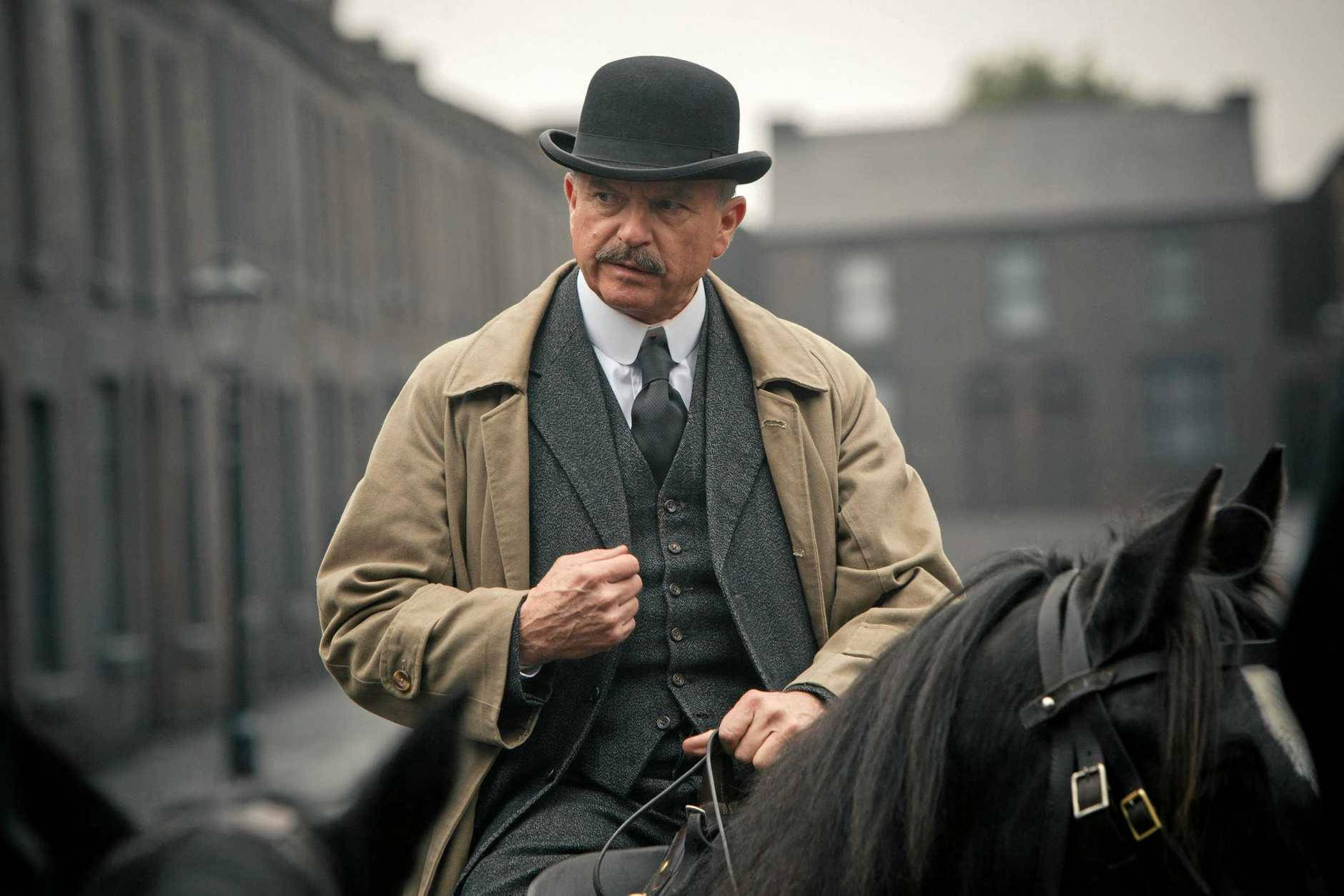 穿著復古服裝的男子騎著黑馬穿過霧氣瀰漫的都市街道。 — Peaky Blinders 壁紙