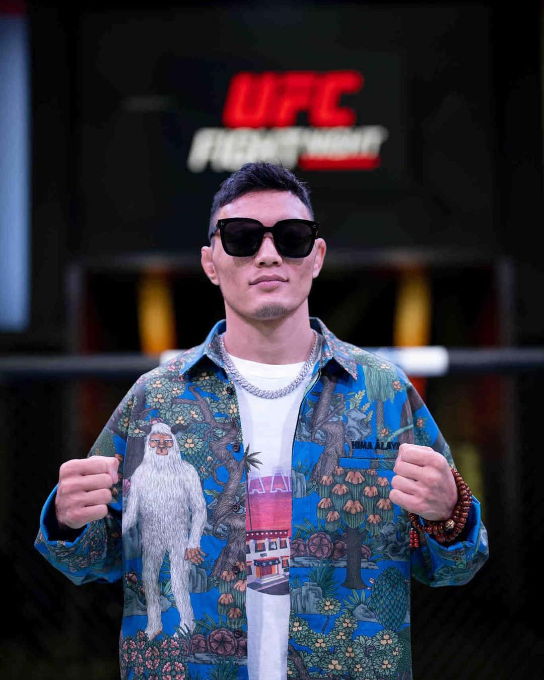 UFC 桌布 壁紙 — 一名戴著太陽眼鏡、身穿鮮豔圖案襯衫的拳手，在UFC Fight Night標誌下自信地舉起拳頭擺姿勢。
