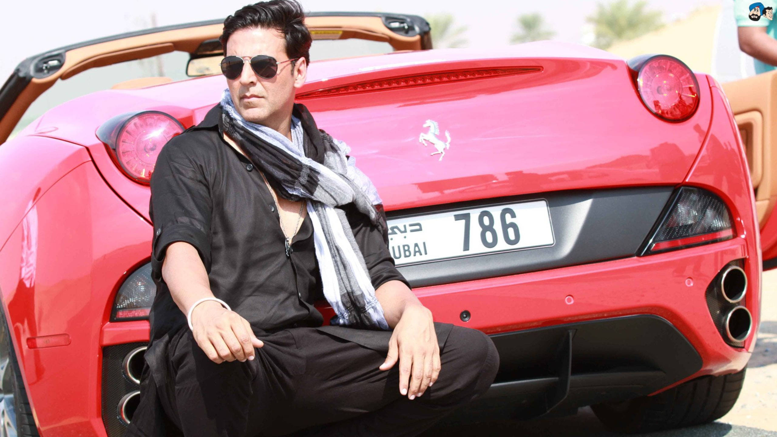 Akshay Kumar 桌布 壁紙 — 一名戴著太陽眼鏡和圍巾的男子，在明亮的日光下自信地坐在一輛掛有杜拜車牌的紅色法拉利旁邊。