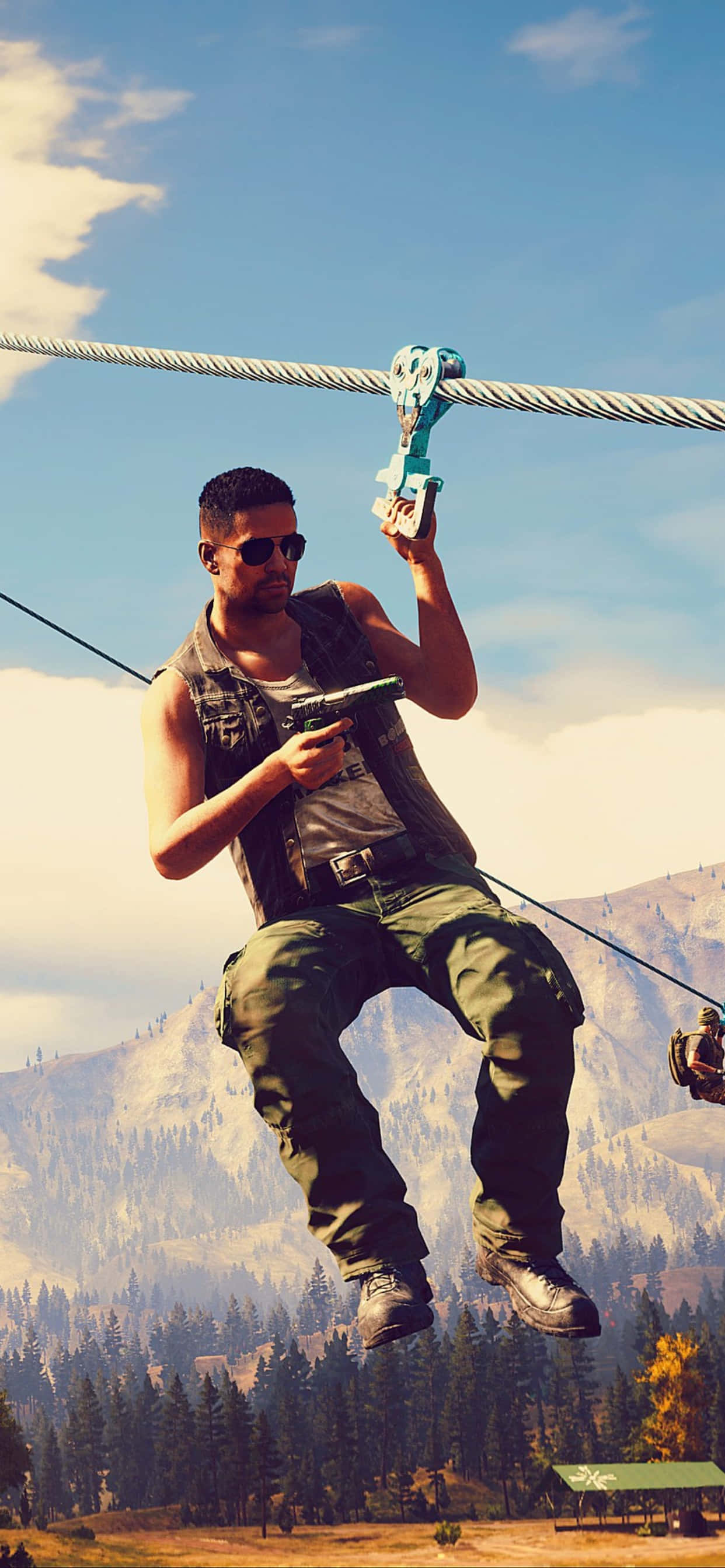 iPhone Xs Max Far Cry 5 桌布 壁紙 — 一名戴著太陽眼鏡和背心的男子，在明亮的藍天下，手持槍枝，沿著鋼索滑過多山的森林。