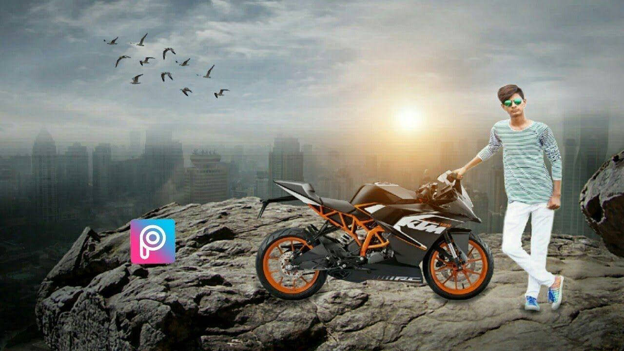 KTM 摩托車 桌布 壁紙 — 一名戴著太陽眼鏡的年輕男子站在黑色和橙色的KTM機車旁，位於岩石懸崖上，俯瞰著日落時分霧氣瀰漫的城市景觀，鳥兒在頭頂飛翔。