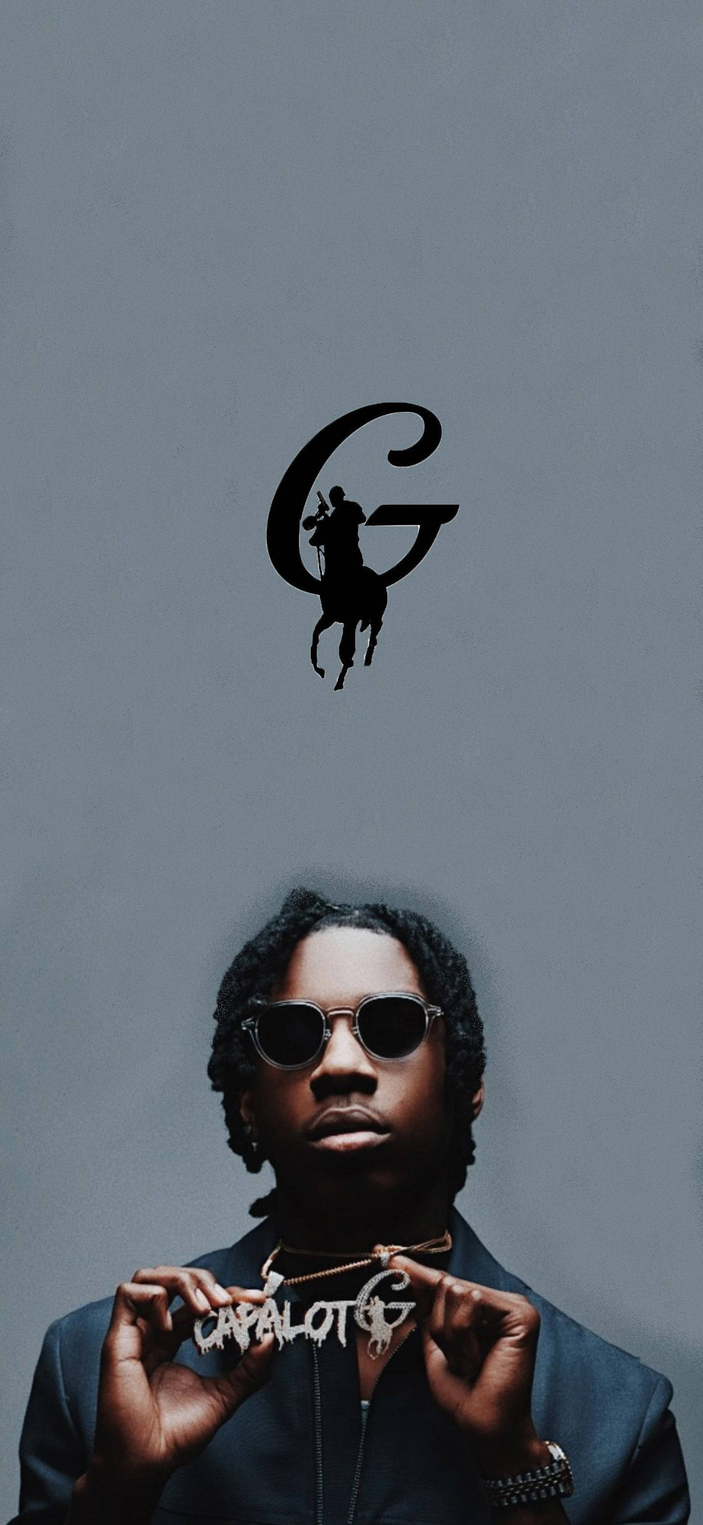 Polo 桌布 壁紙 — 一名戴著太陽眼鏡的男子，在一個大型風格化「G」標誌（標誌上有一個騎馬的騎士，背景為柔和的灰色）下方，手持一條「CAPALOT G」項鍊。