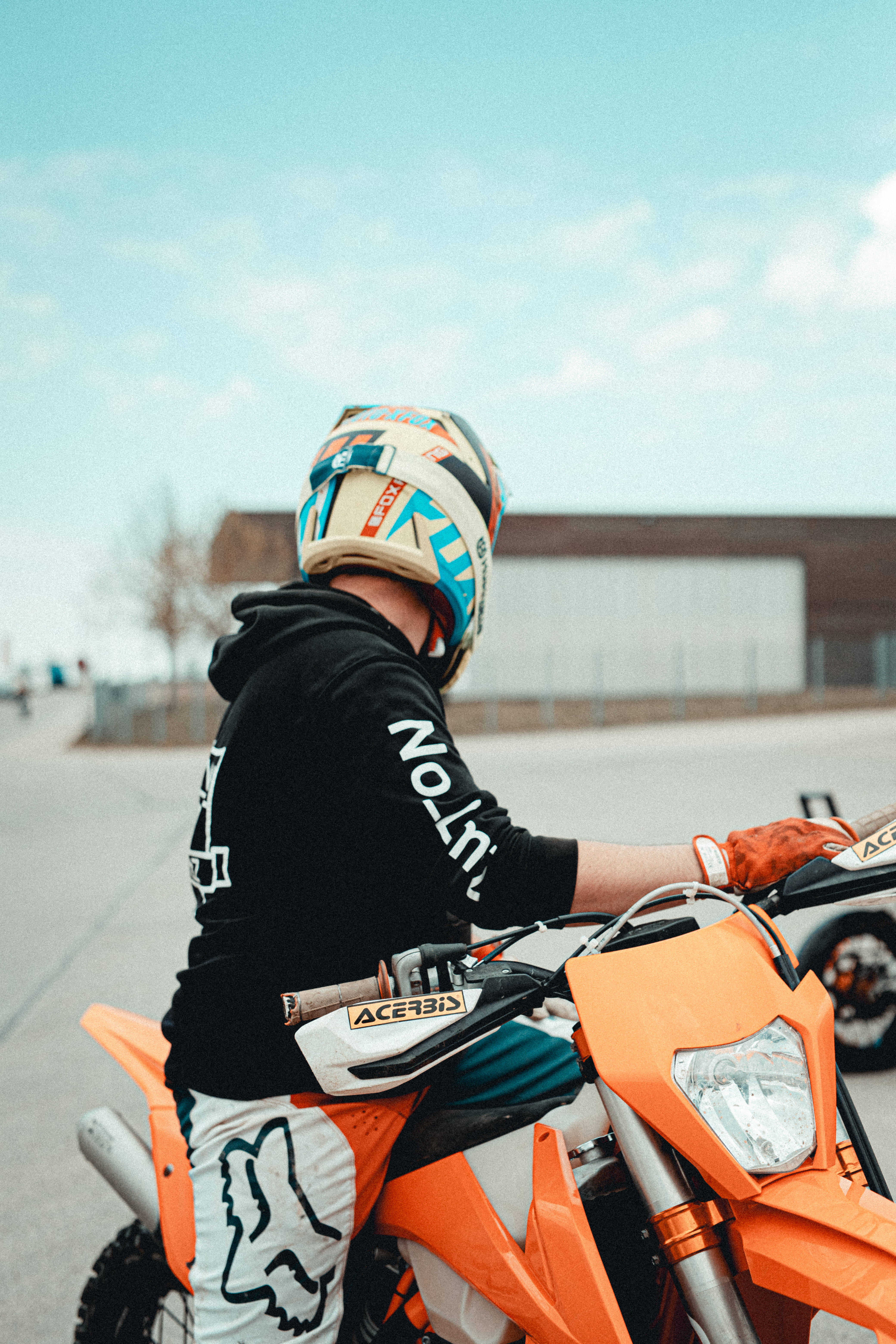Ktm Bike 桌布 壁紙 — 一名戴著彩色頭盔的騎士坐在一輛亮橙色越野車上，在開闊的鋪砌區域，天空清澈湛藍。