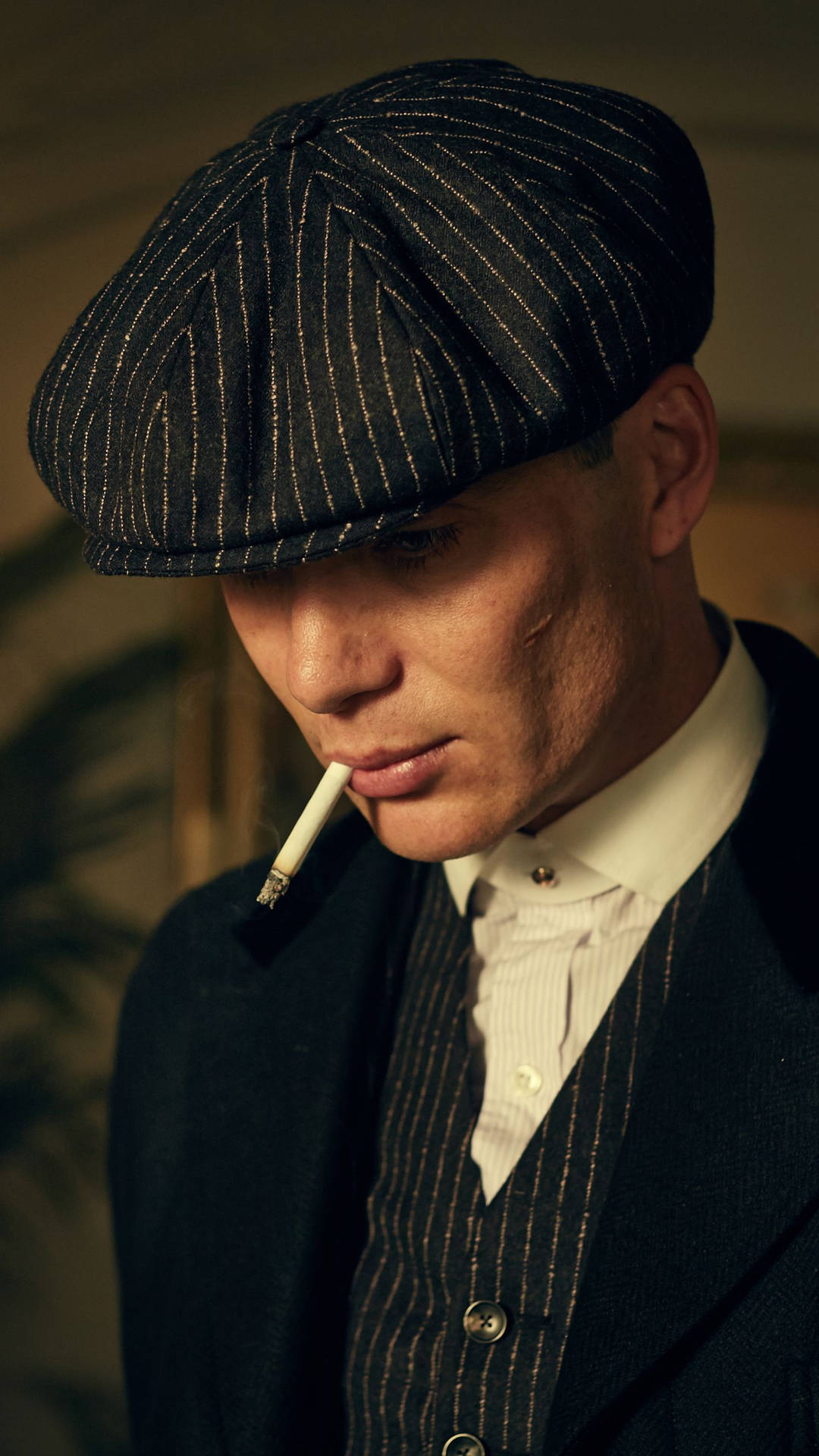 穿著條紋西裝和帽子的男子抽煙，表情嚴肅。 — Peaky Blinders 壁紙