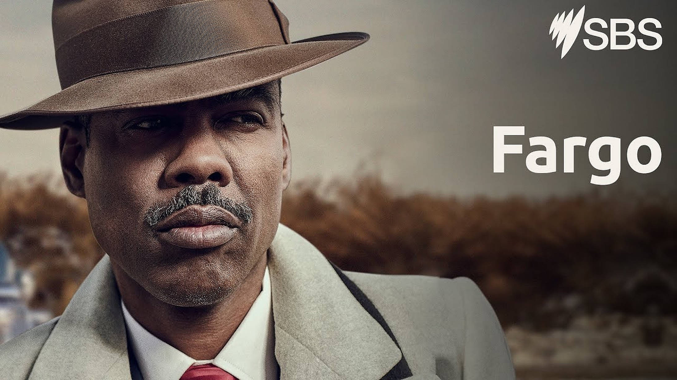 Chris Rock 桌布 壁紙 — 一名戴著棕色軟呢帽、身穿灰色外套的男子，在帶有 'Fargo' 文字的柔和秋日背景下專注凝視。