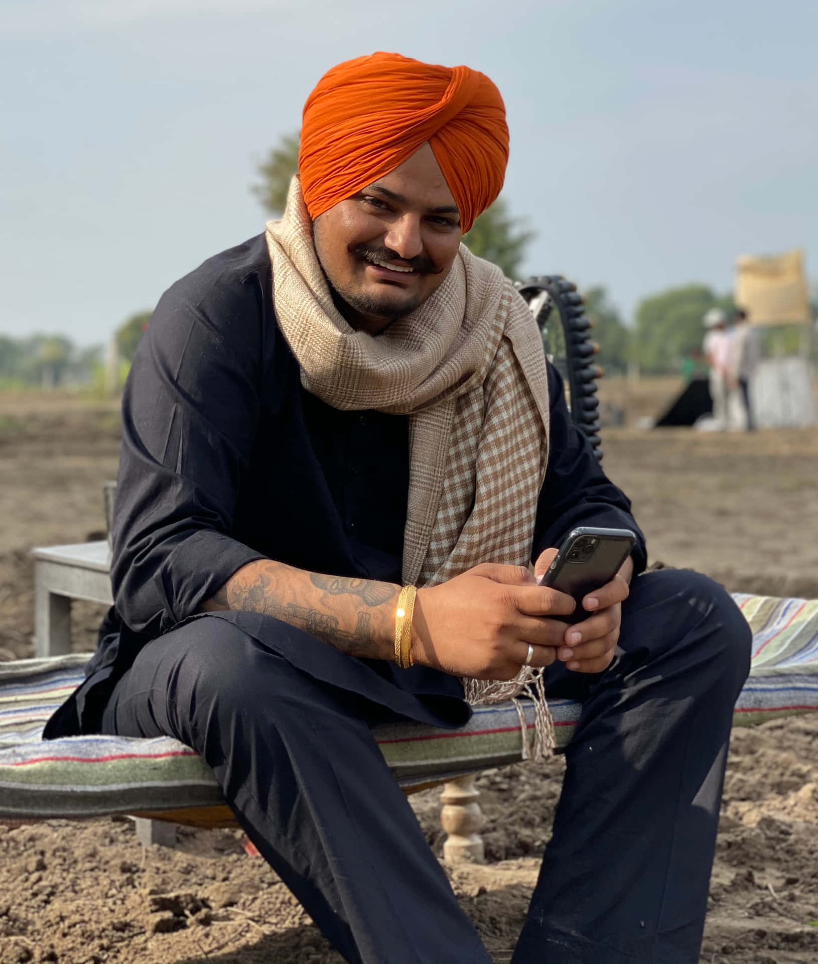 戴橙色頭巾的男子微笑著在戶外使用手機 — Sidhu Moose Wala 壁紙