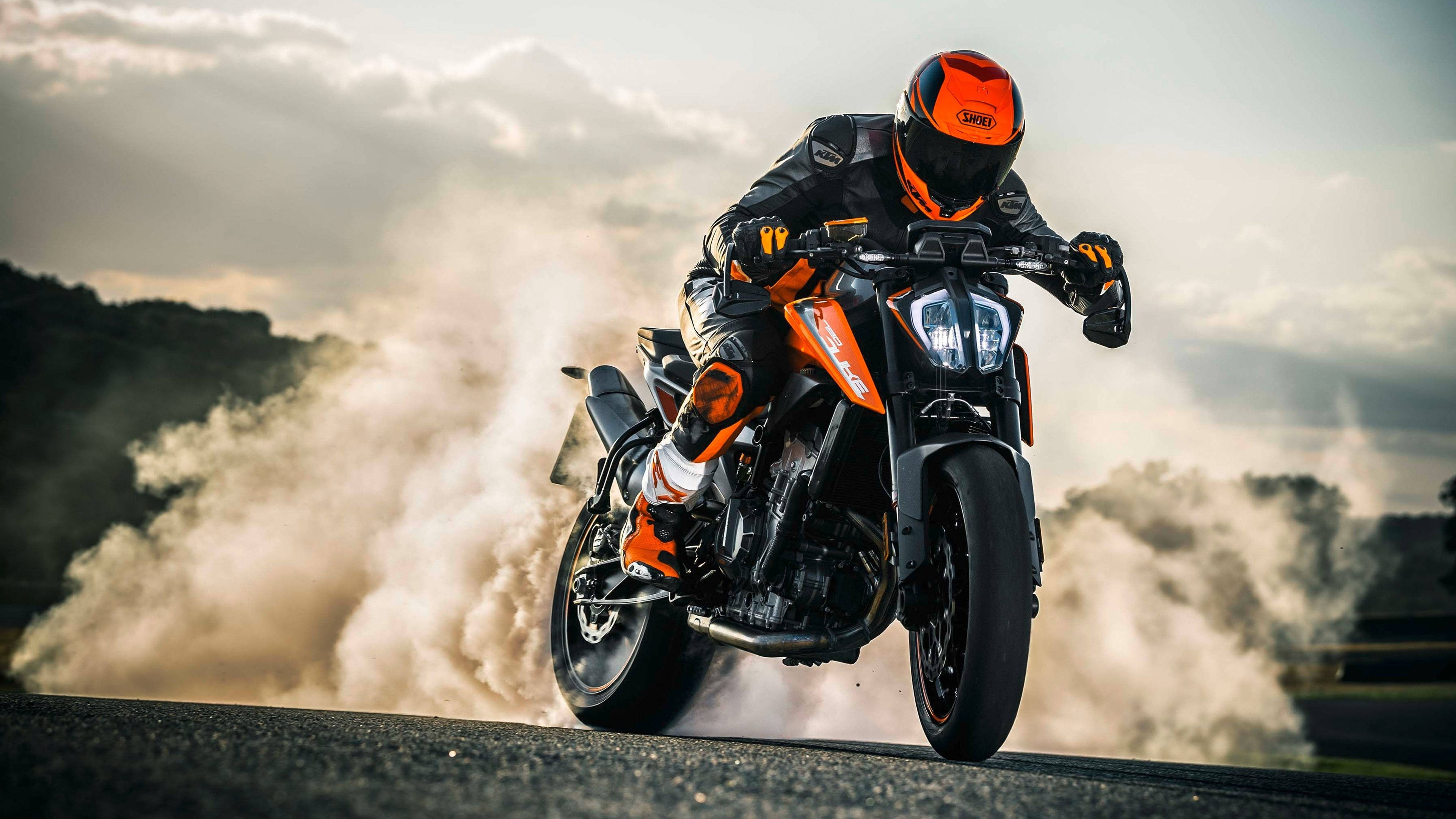 KTM 摩托車 桌布 壁紙 — 一名戴著橙色頭盔和裝備的騎士，在橙色和黑色的KTM摩托車上傾斜入彎，在蜿蜒的道路上揚起灰塵。