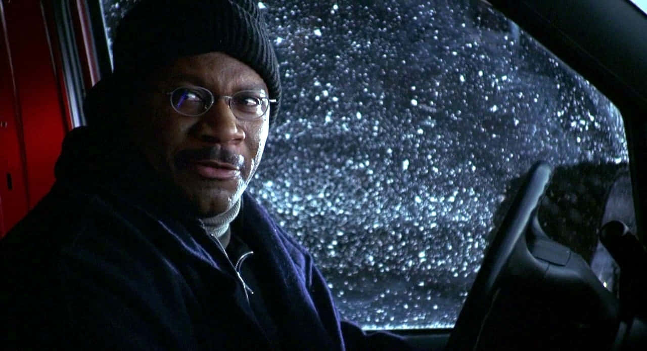 Ving Rhames 桌布 壁紙 — 一名戴著毛帽和眼鏡的男子在車內凝視前方，雪花在夜間劃過擋風玻璃。