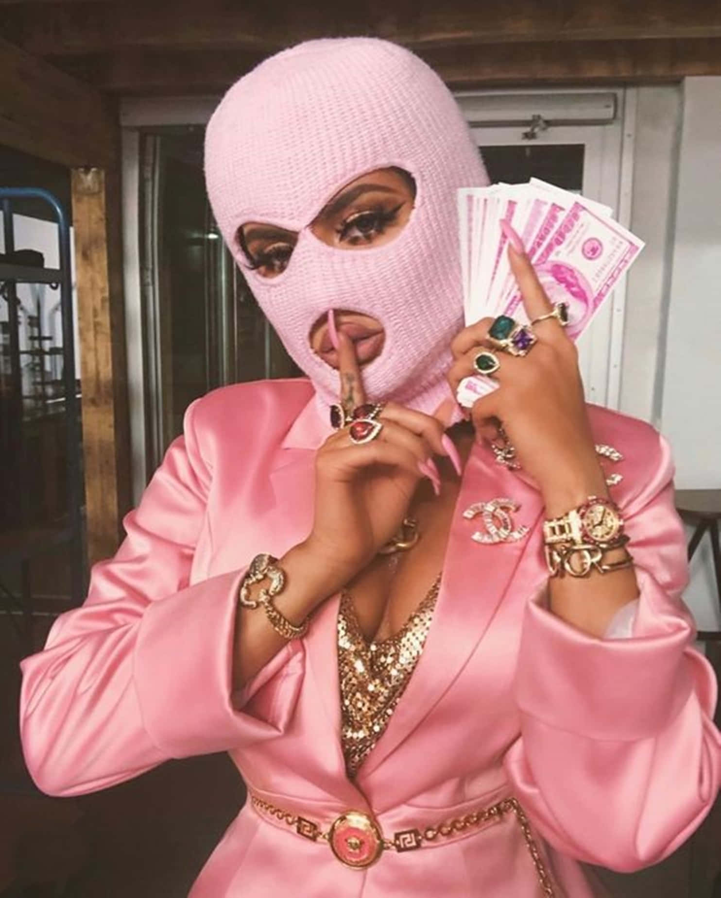 Baddie Girl 桌布 壁紙 — 一名戴著粉紅色巴拉克拉瓦帽、身穿相配緞面西裝的人，手持扇狀現金，並用戴有珠寶的手做出噤聲手勢。