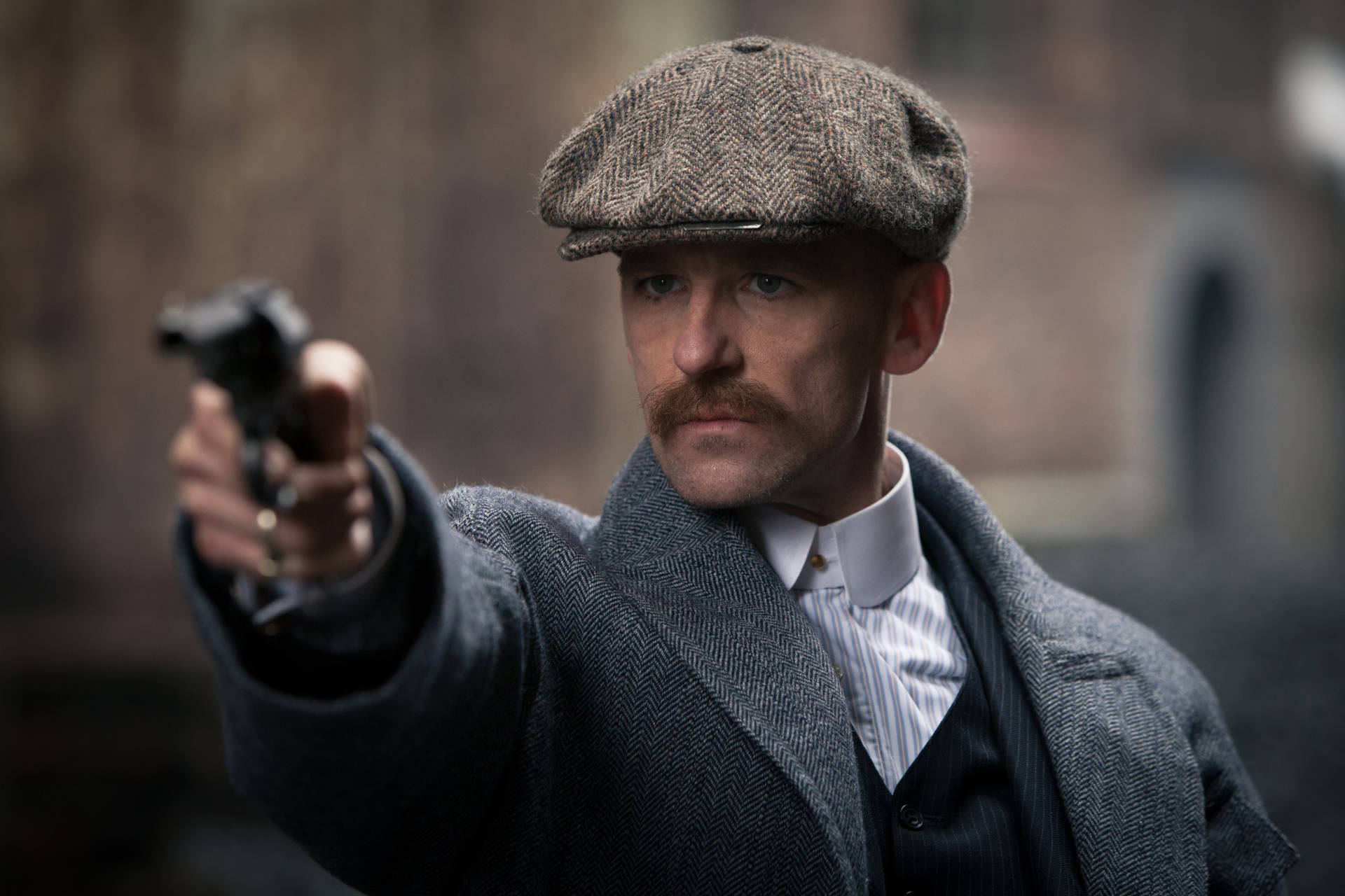 身穿復古外套和帽子的男子，表情嚴肅地瞄準手槍。 — Peaky Blinders 壁紙