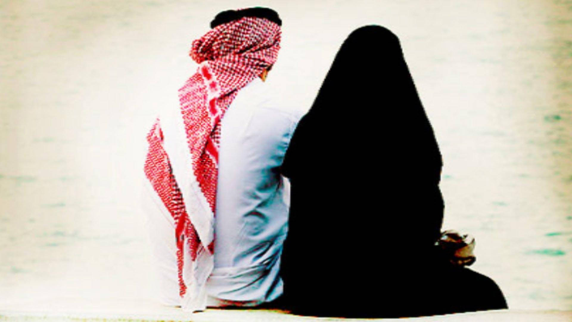 muslim 桌布 壁紙 — 一名戴著紅白格紋頭巾的男子與一名穿著黑色長袍的女子並肩坐在淺色紋理表面上，兩人都背對鏡頭。
