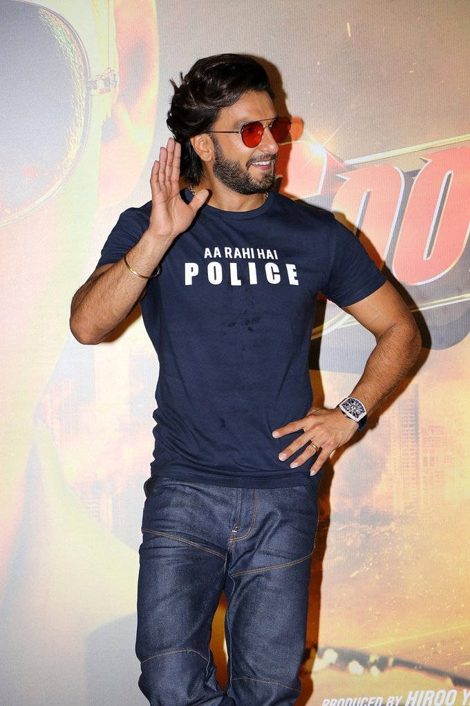 Ranveer Singh 桌布 壁紙 — 一名戴著紅色太陽眼鏡、身穿海軍藍色「AARAH HAI POLICE」T恤的男子在宣傳活動中愉快地揮手。