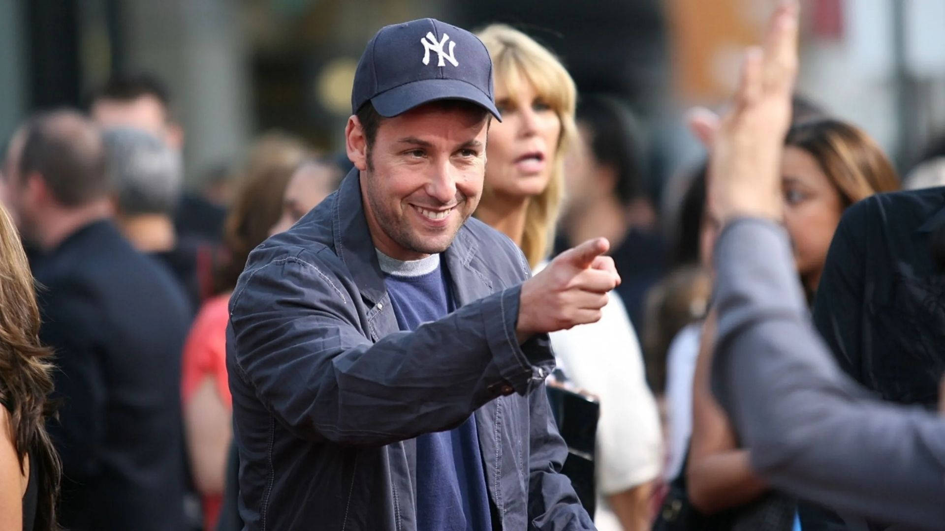 Adam Sandler 桌布 壁紙 — 一名戴著紐約洋基隊帽子的微笑男子，在熙攘的人群中向粉絲揮手。