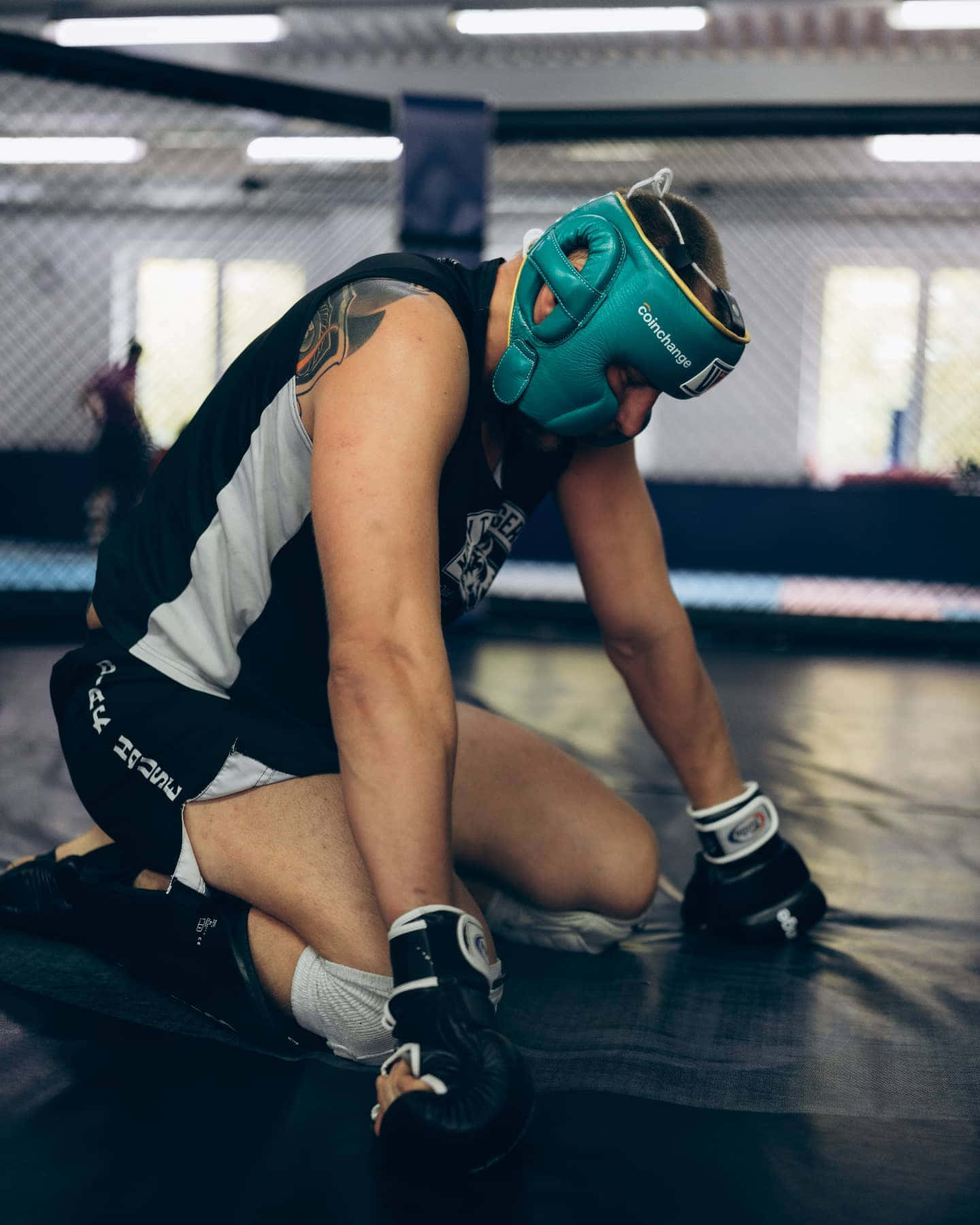 Athletic 桌布 壁紙 — 一名戴著綠色頭盔的戰士在圍欄健身房內的深色墊子上，經過激烈訓練後疲憊地跪著。