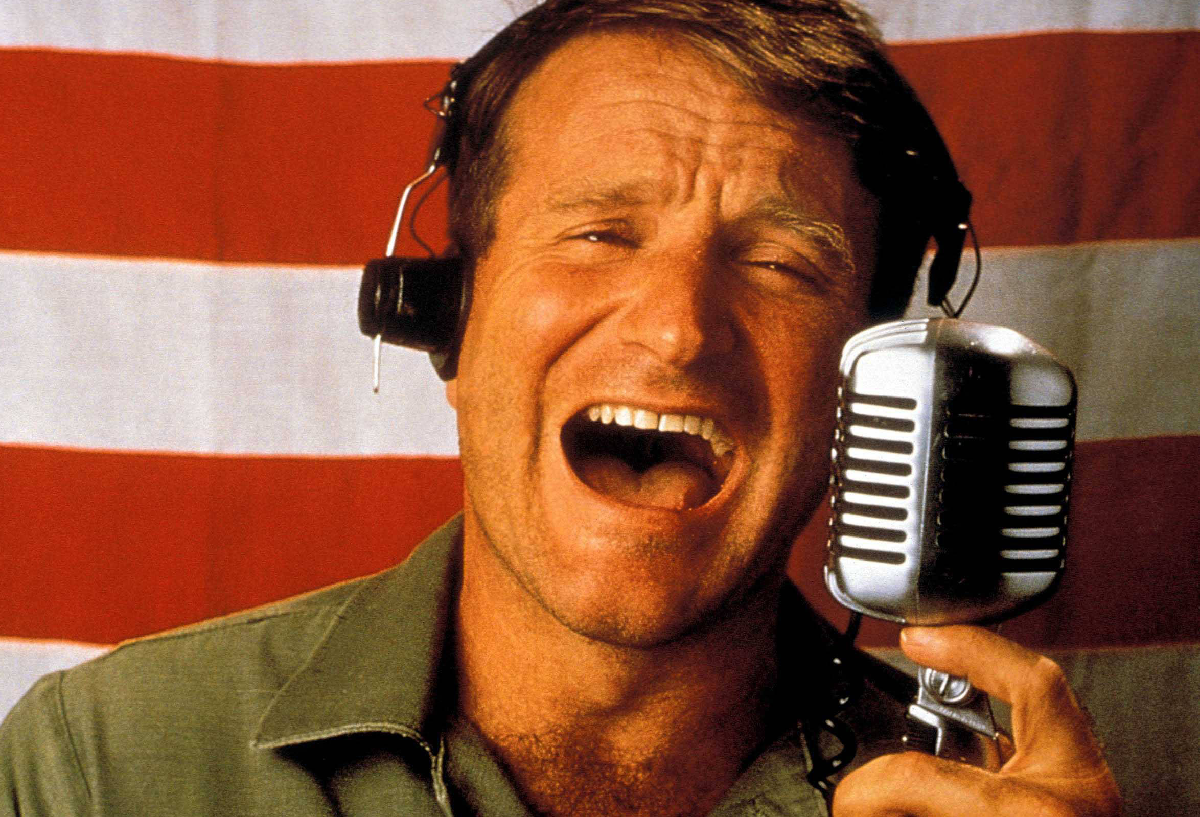 robin williams 桌布 壁紙 — 一名戴著耳機的男子對著復古銀色麥克風開懷大笑，背景是美國國旗。