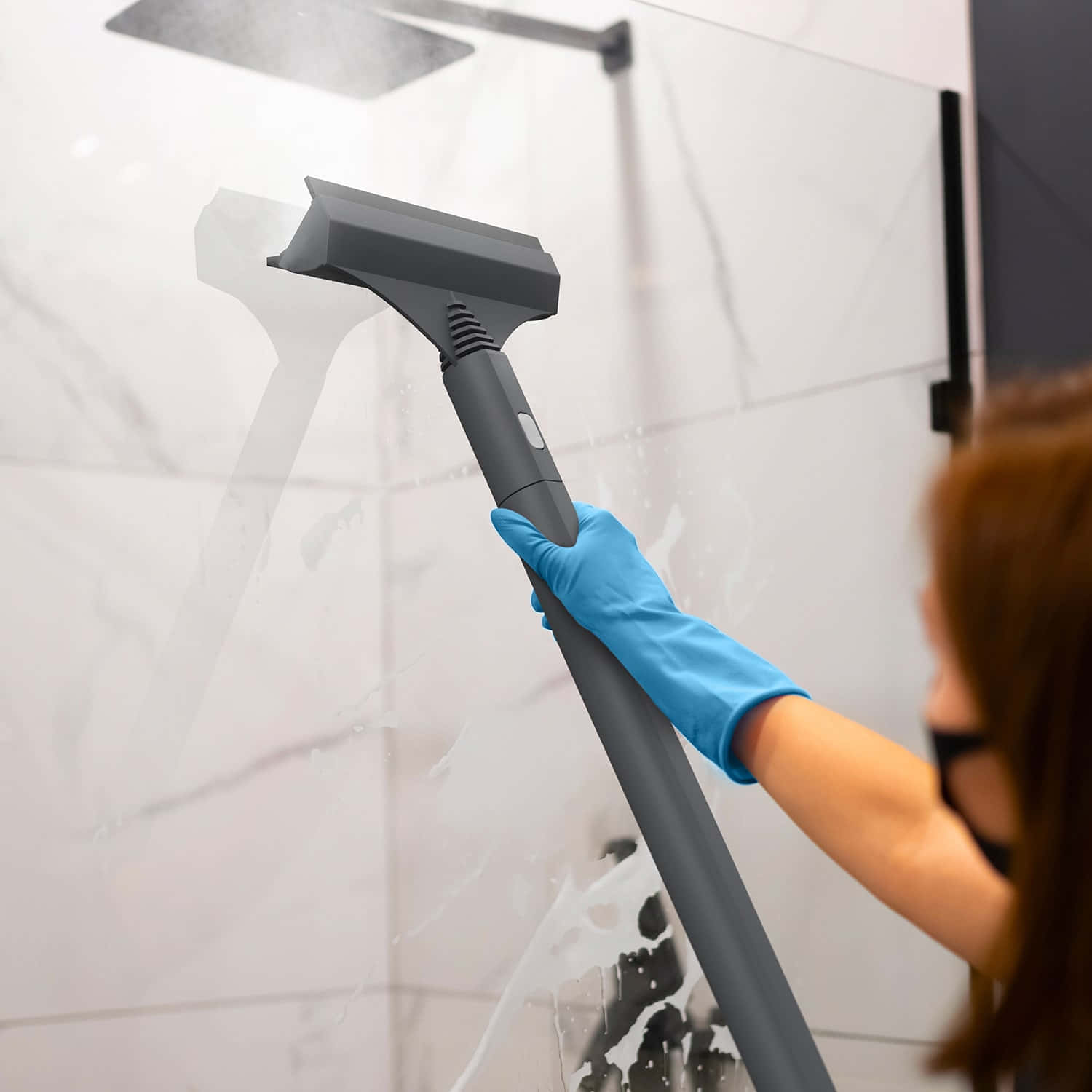 Cleaning 桌布 壁紙 — 一名戴著藍色手套的人用灰色刮水器清潔現代淋浴間白色大理石瓷磚上的肥皂水。