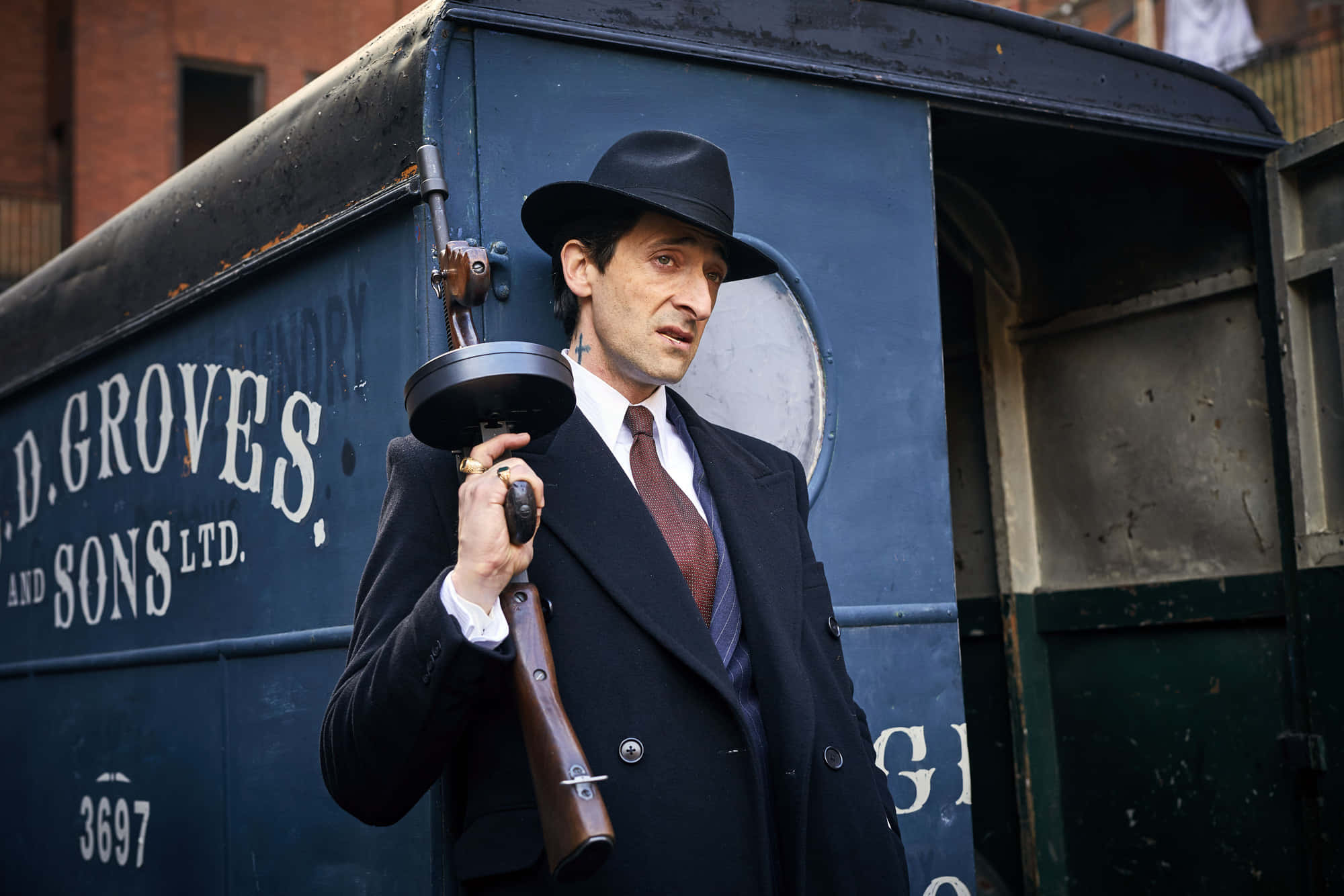 戴軟呢帽穿西裝的男子拿著霰彈槍，旁邊是藍色貨車。 — Peaky Blinders 壁紙