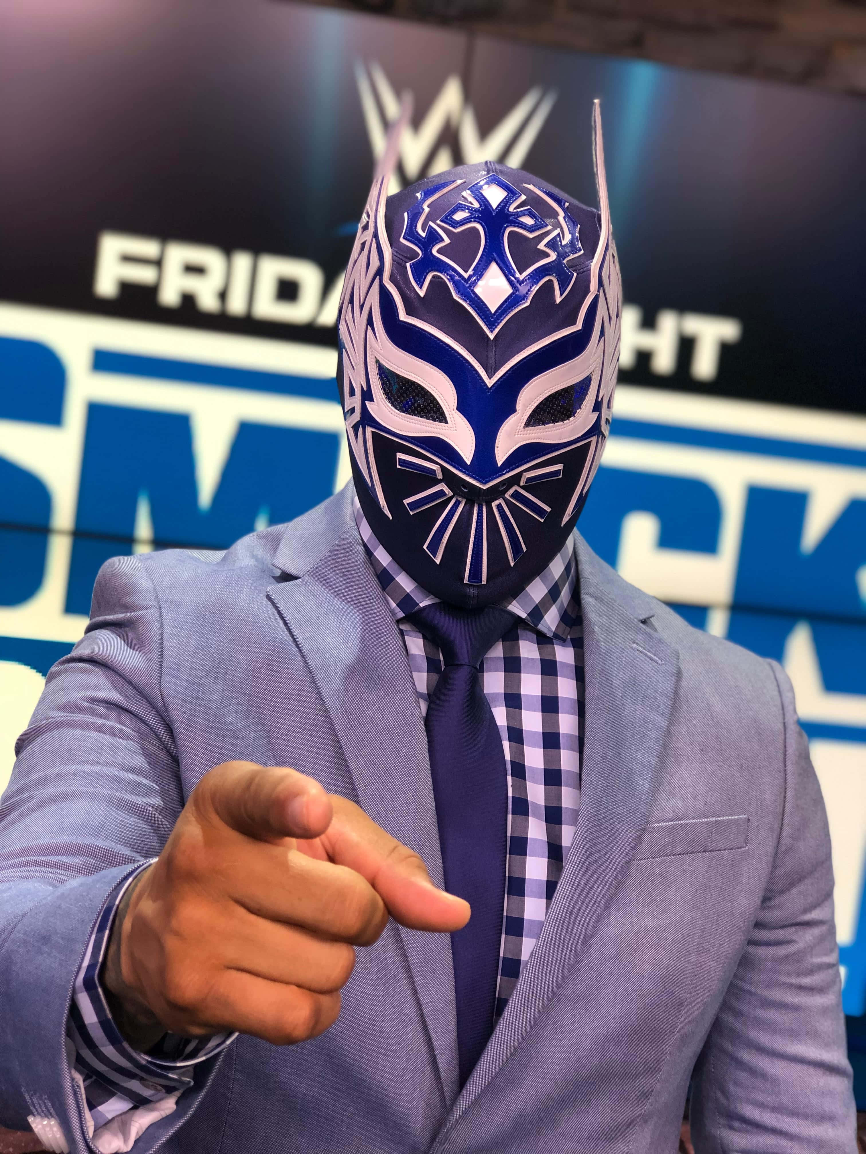 WWE 桌布 壁紙 — 一名戴著面具的摔角手身穿筆挺西裝，在WWE Friday Night SmackDown背景下直接指向觀眾。