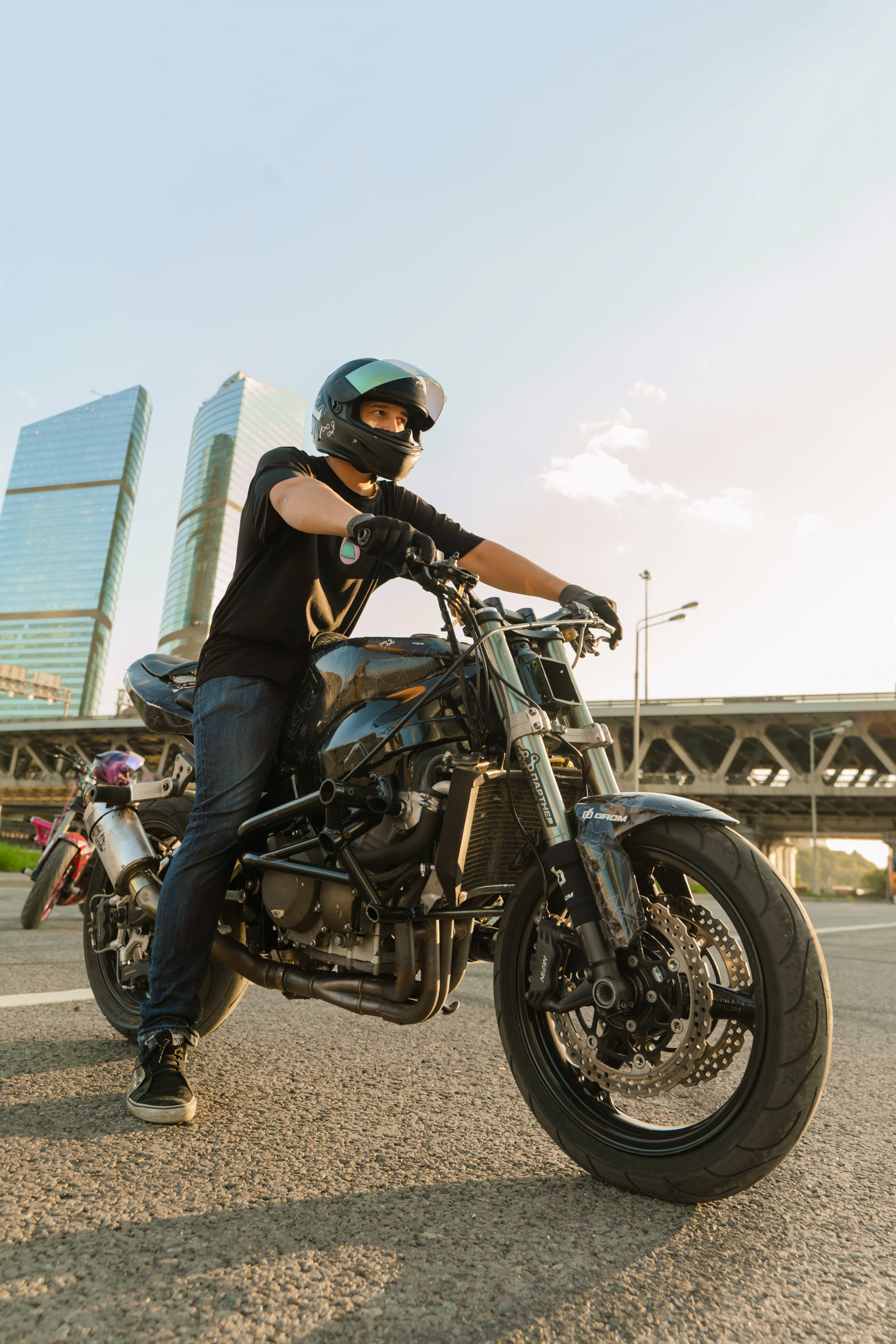 Man Aesthetic 桌布 壁紙 — 一名戴著頭盔的摩托車手在黃金時段，以現代摩天大樓為背景，自信地在一輛訂製摩托車上擺姿勢。