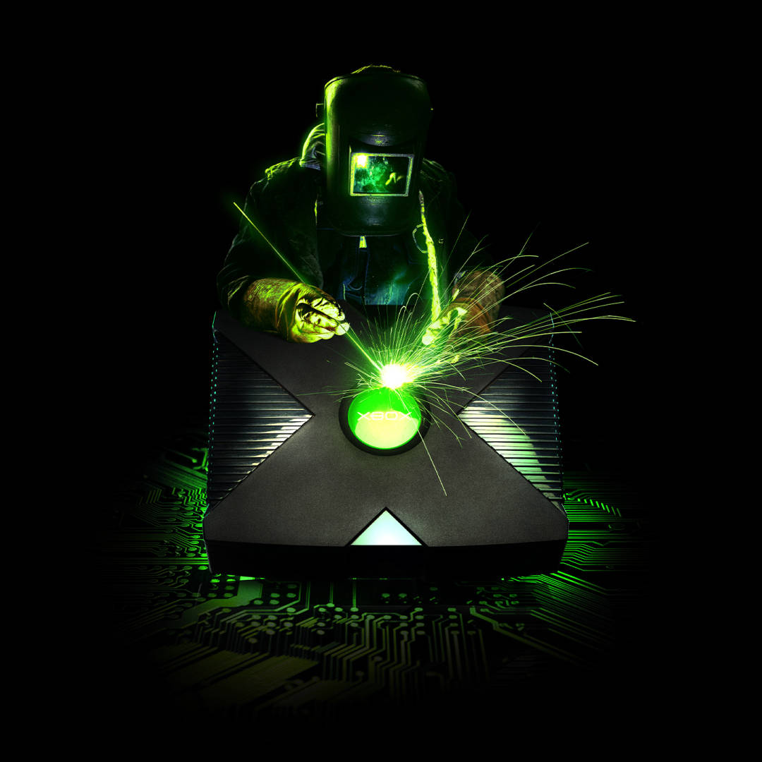 Xbox 桌布 壁紙 — 一名戴著頭盔的焊工在黑暗的電路板背景下，將Xbox標誌焊接在遊戲機上，發出綠色光芒。