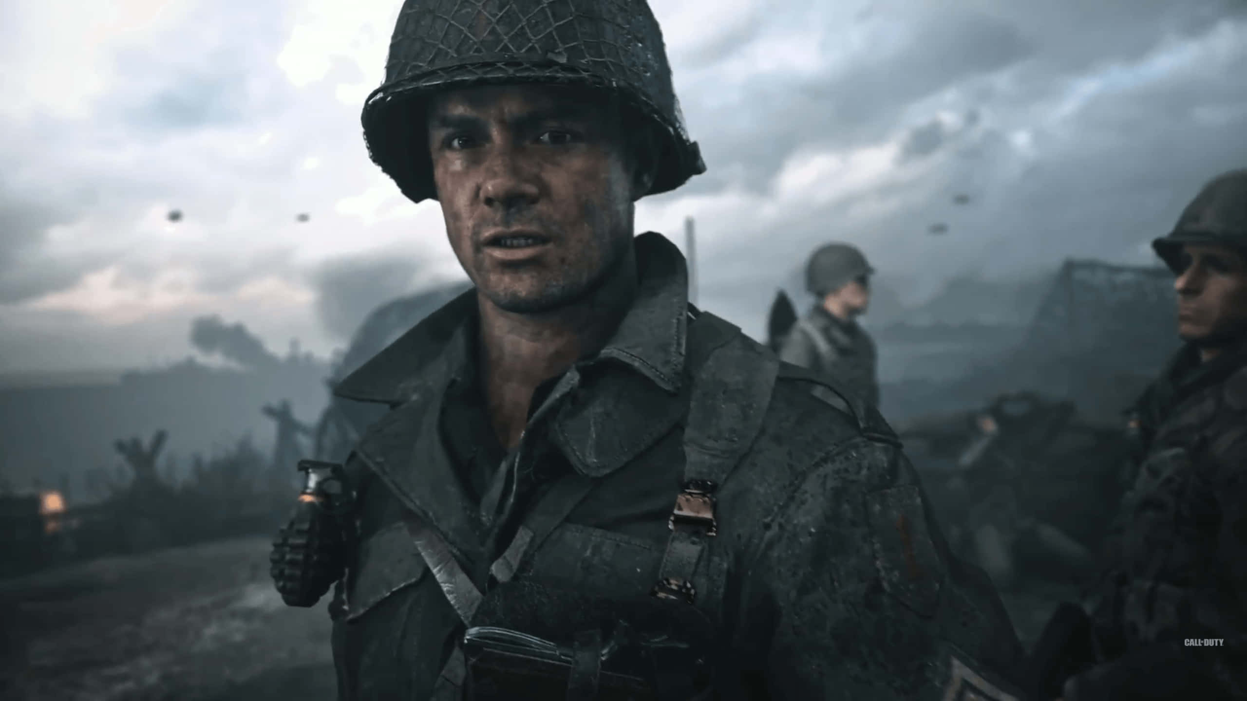 World War 2 桌布 壁紙 — 一名戴著頭盔的疲憊士兵，在煙霧瀰漫的戰場上專注地凝視，背景有其他部隊。