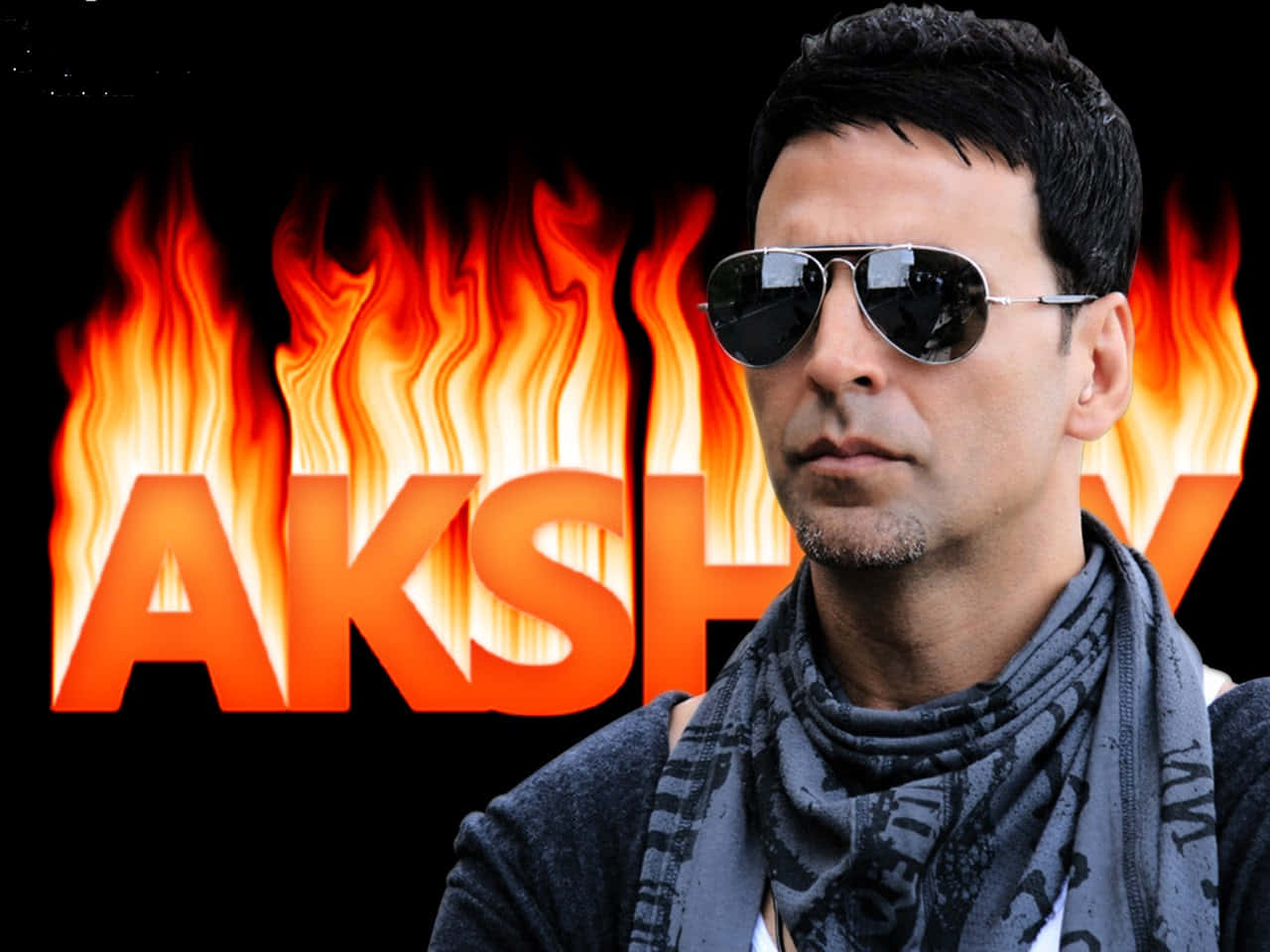 Akshay Kumar 桌布 壁紙 — 一名戴著飛行員太陽眼鏡和圍巾的男子站在熾熱的橙色火焰前，他的名字在他身後發光。