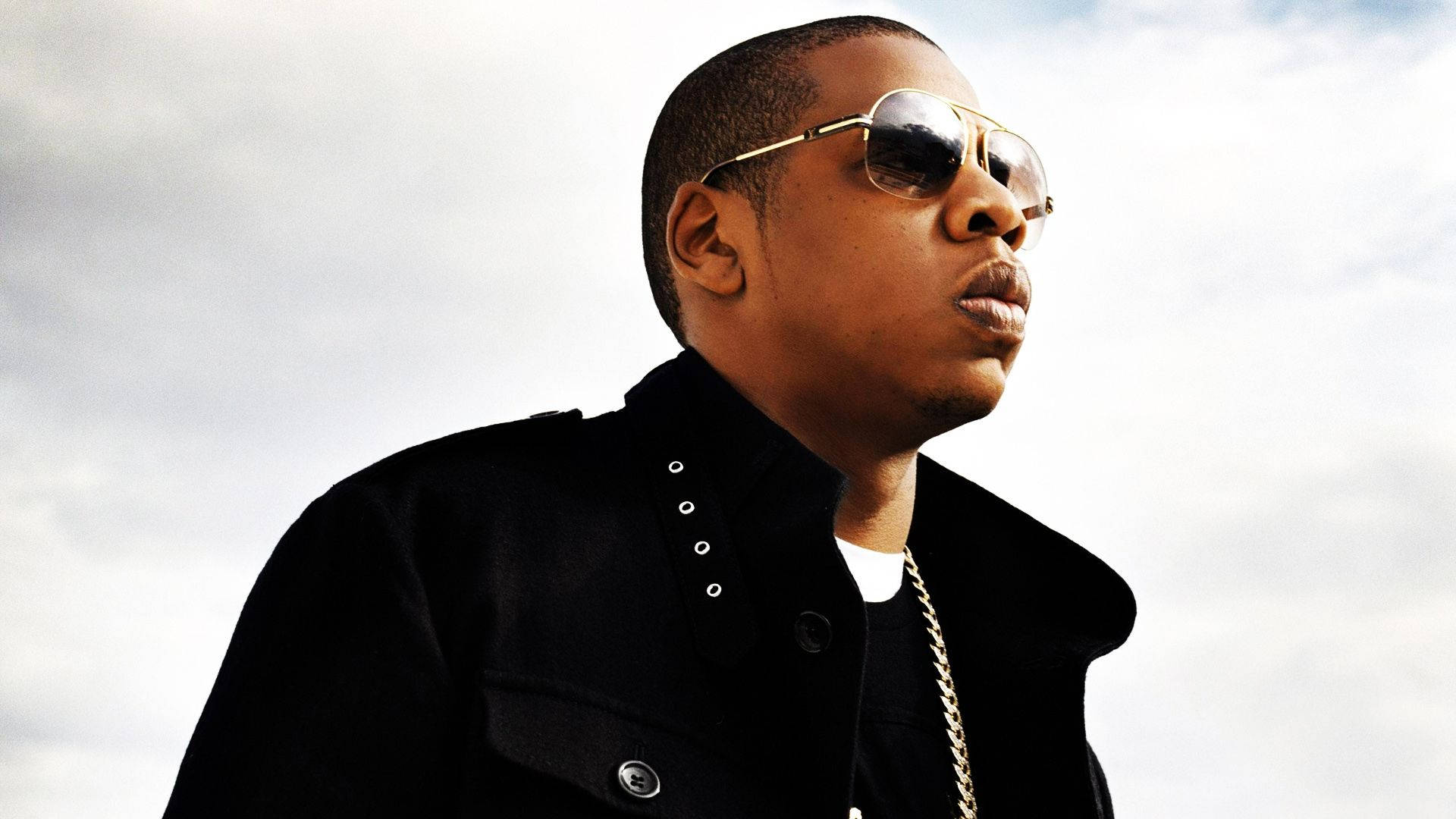 Jay-z 桌布 壁紙 — 一名戴著飛行員太陽眼鏡和黑色外套的男子，在陰天自信地擺姿勢。