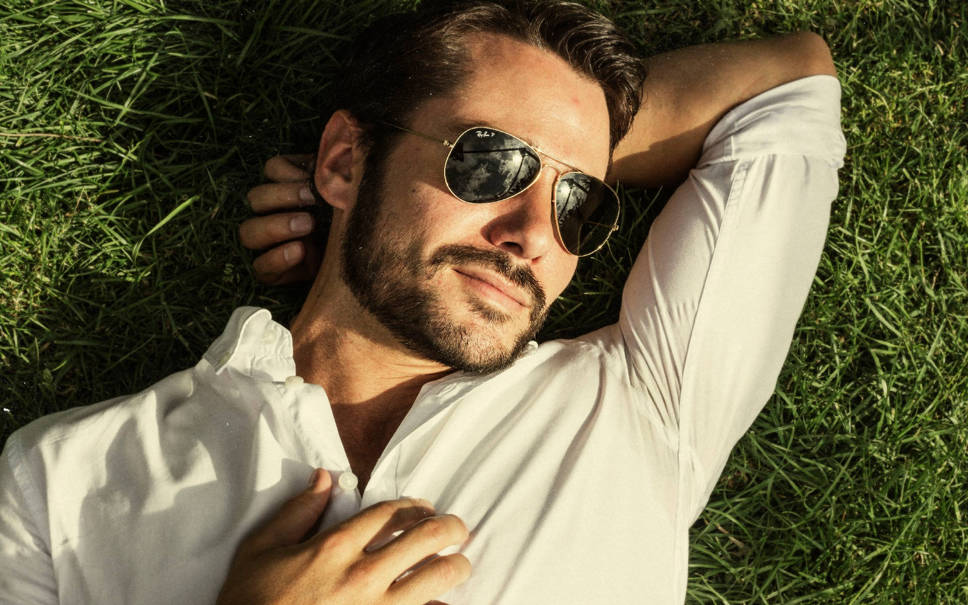 Sunglasses 桌布 壁紙 — 一名戴著飛行員太陽眼鏡的男子，穿著白色襯衫，在陽光照耀的綠色草地上放鬆休息。