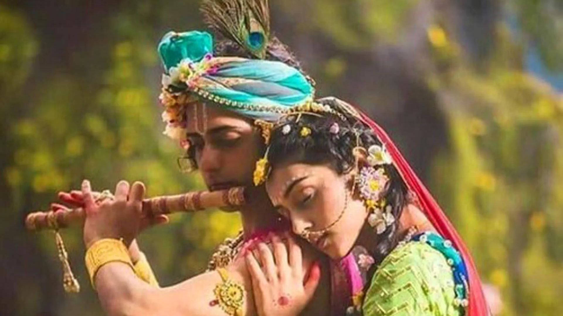 radha krishna serial 桌布 壁紙 — 一名戴著鮮藍色頭巾的男子吹奏長笛，一名身穿綠色服飾的女子在金色樹葉中將頭靠在他的肩膀上。