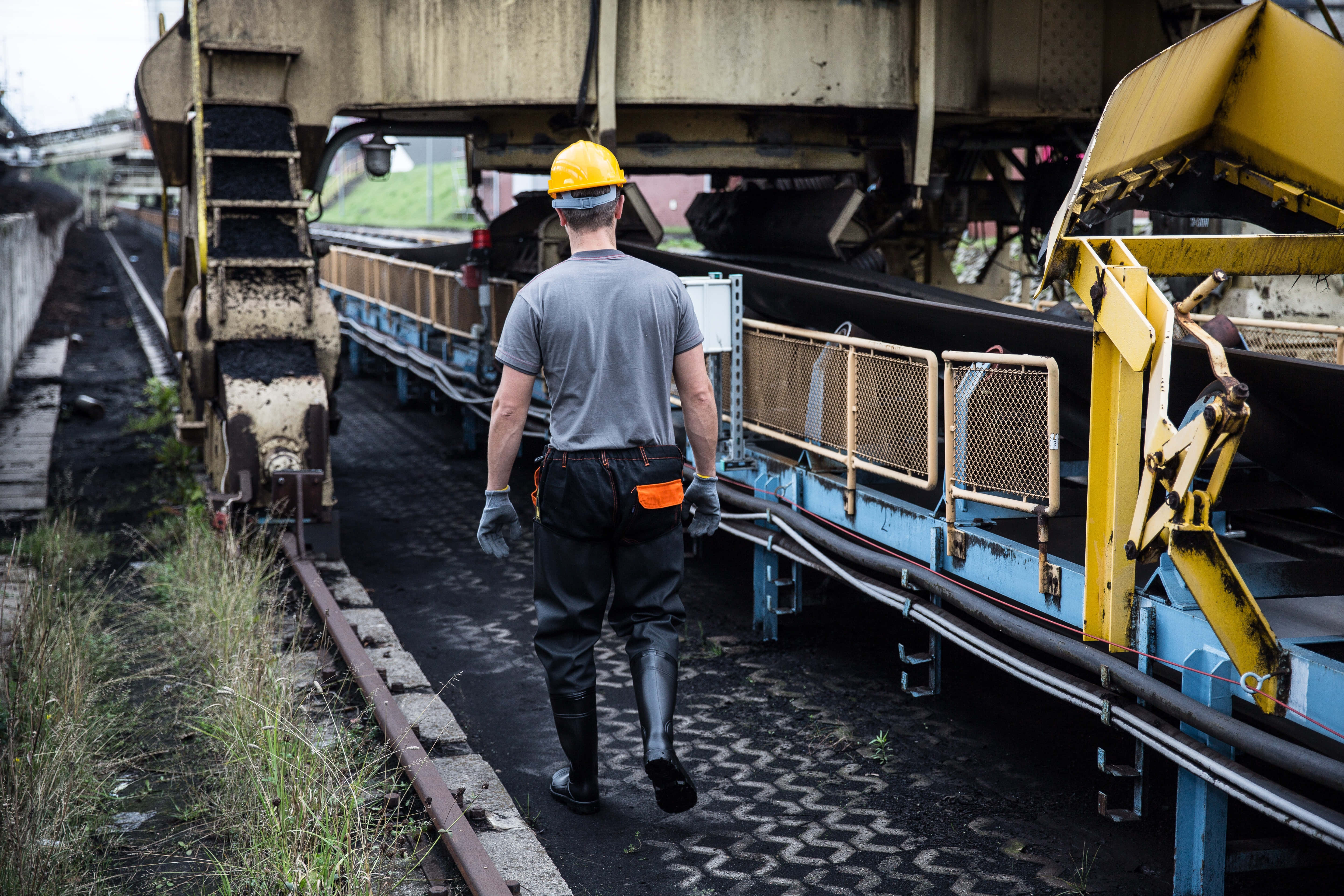 Mining 桌布 壁紙 — 一名戴著黃色安全帽的工人沿著工業採礦設施的煤炭輸送帶行走。