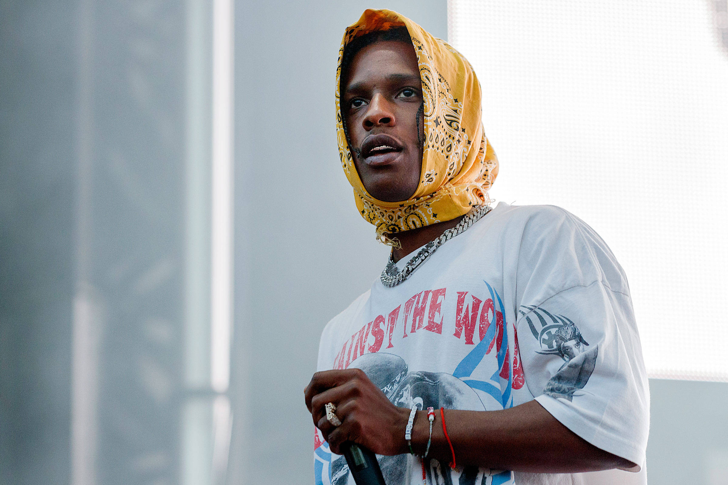 rocky 桌布 壁紙 — 一名戴著黃色頭巾和圖案T恤的男子在明亮的白色背景前拿著麥克風。