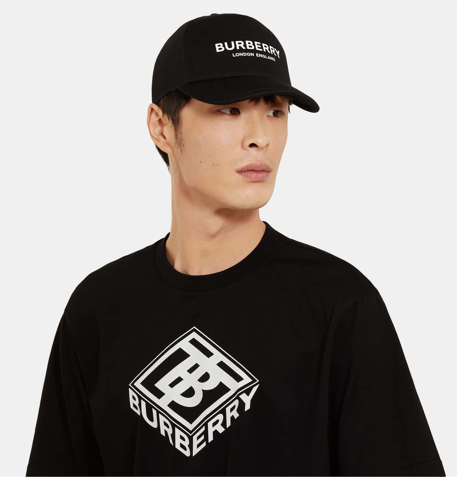 Burberry 桌布 壁紙 — 一名戴著黑色Burberry帽及搭配白色標誌T恤的男子站在純色背景前。