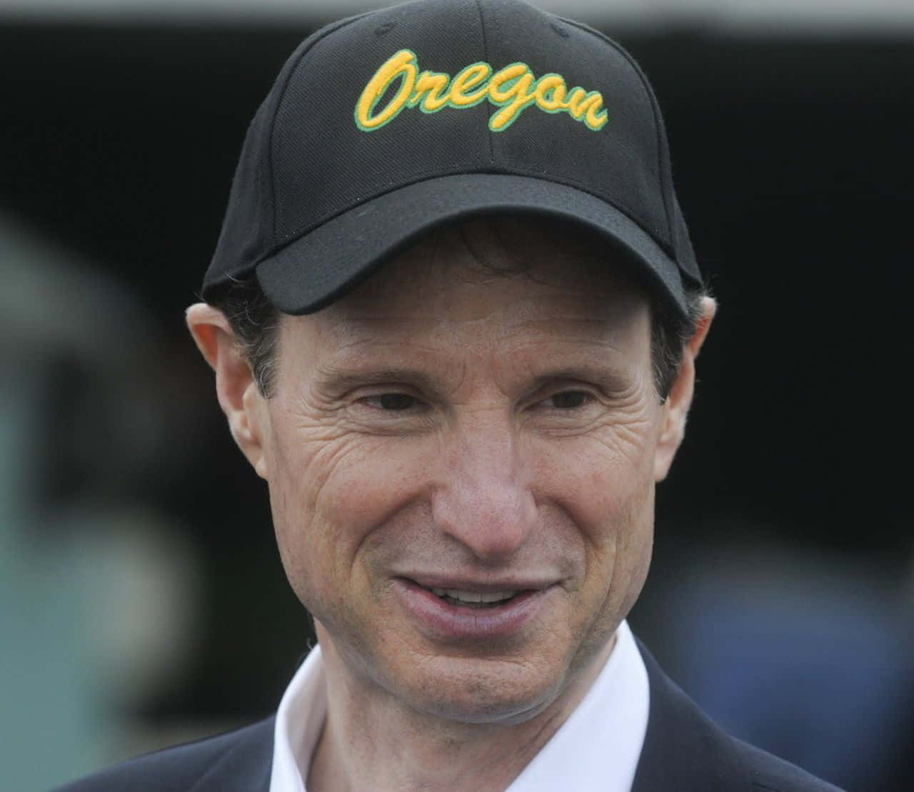 Celebrity 桌布 壁紙 — 一名戴著黑色帽子、上面有黃色「Oregon」字樣的男子特寫，在模糊的背景中微微微笑。